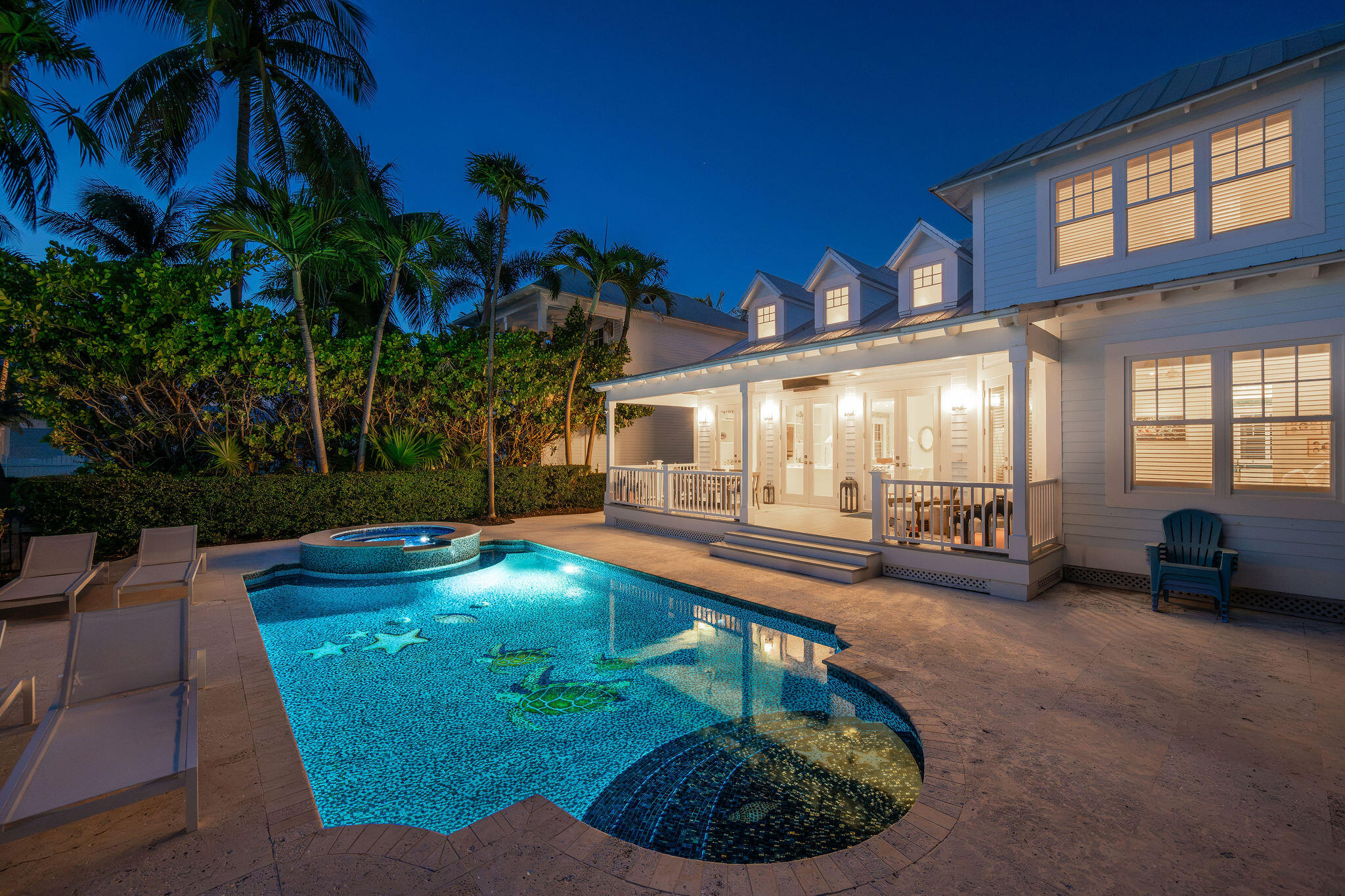 White coastal home glowing at dusk beside a turquoise pool and raised circular spa.