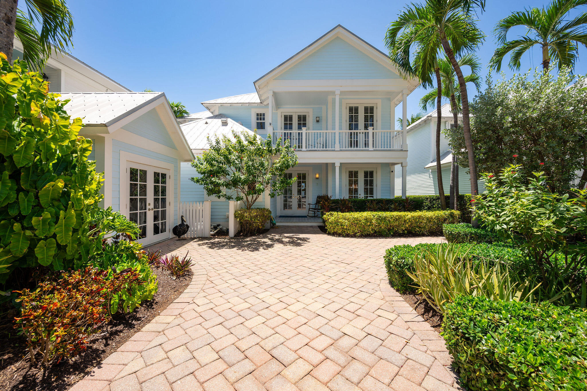 Pale blue two-story home with a white balcony, tropical palms, and a broad paved approach.