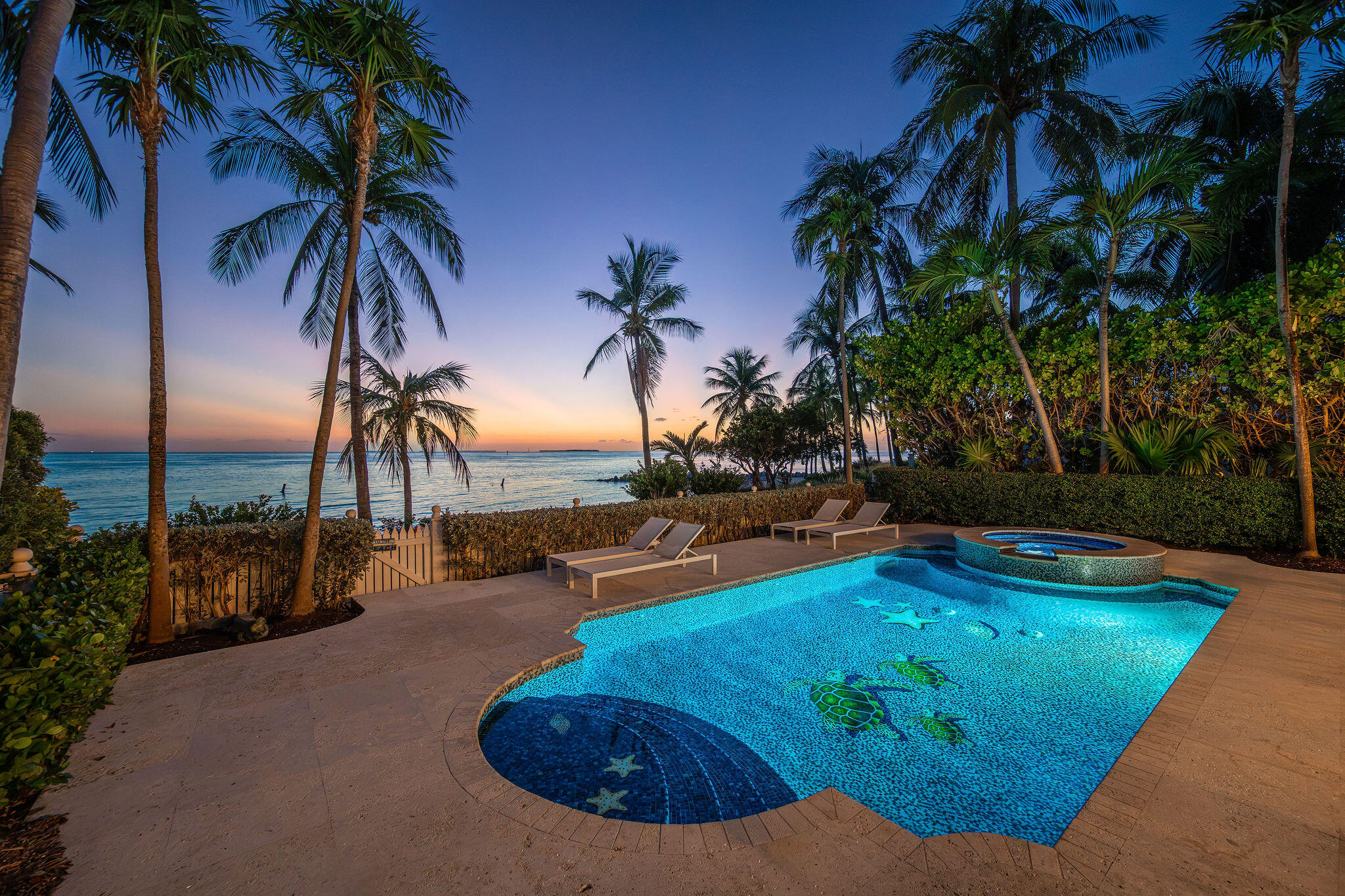 Oceanfront swimming pool and raised spa framed by palms at sunset.