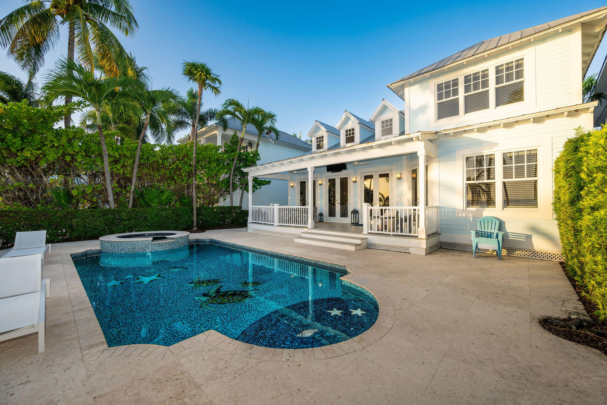White coastal home with a covered porch and a blue pool with raised spa, framed by palm trees.