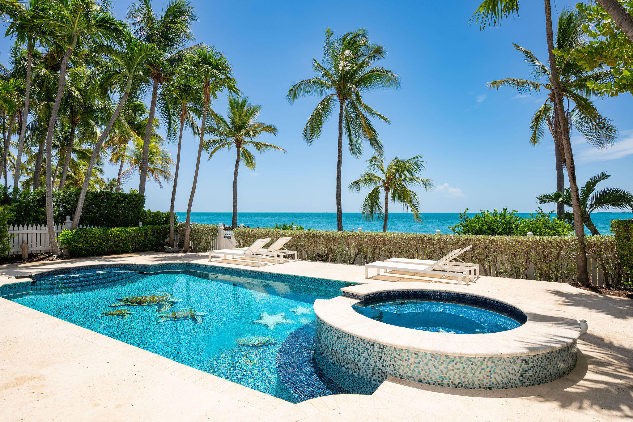 Oceanfront pool and raised spa framed by palm trees, with white lounge chairs along the water.