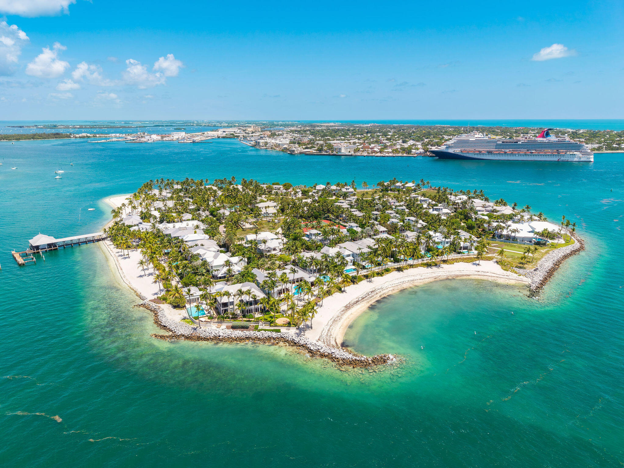 Aerial view of Sunset Key’s palm-lined island, sandy beaches, turquoise water, and a cruise ship across the channel.