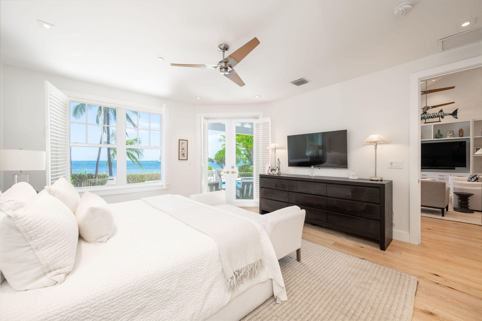 Bedroom with white bedding and plantation-shuttered windows overlooking the ocean.
