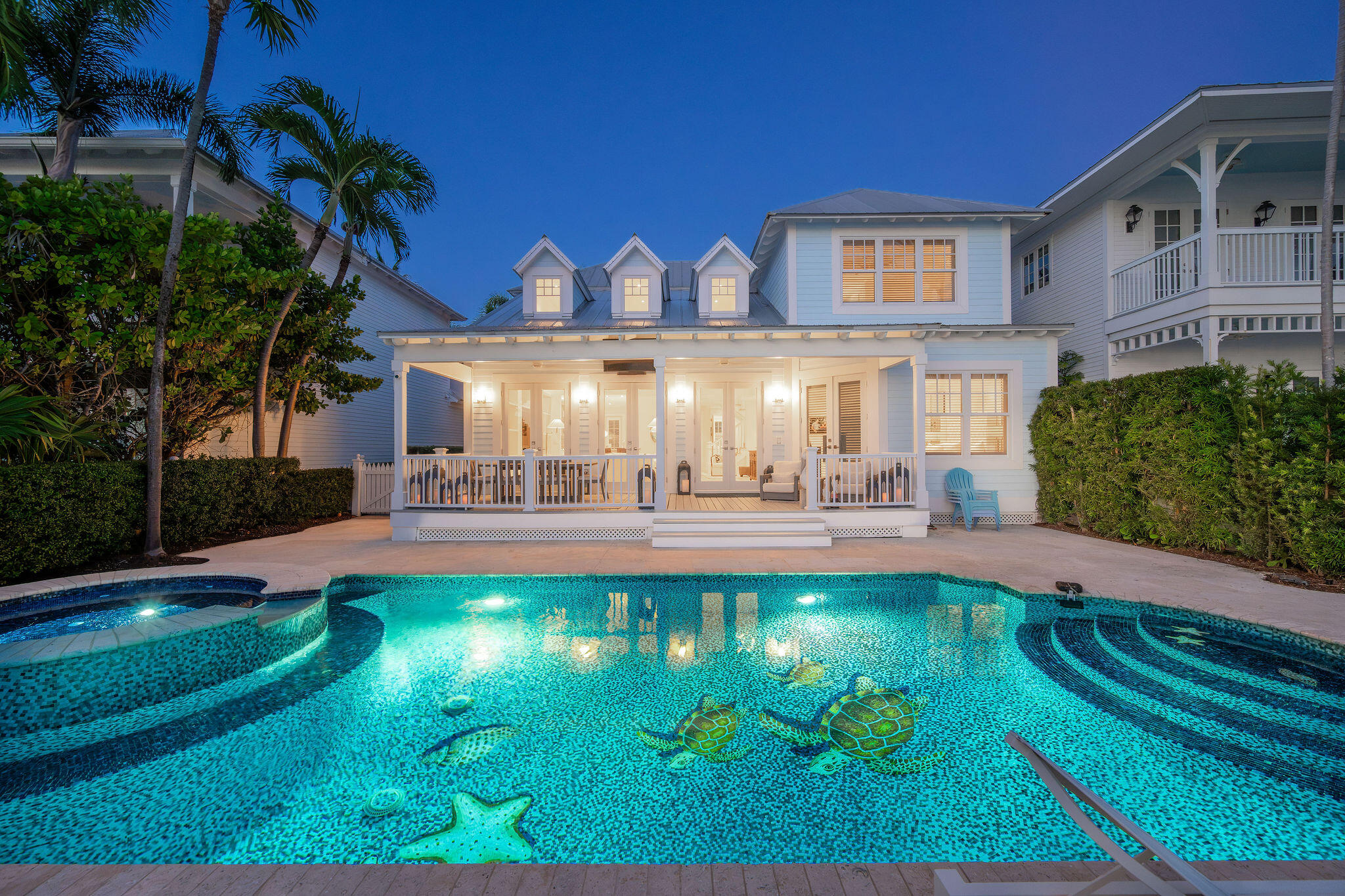 Light-blue two-story house with a covered porch behind a glowing pool with sea-life mosaics.