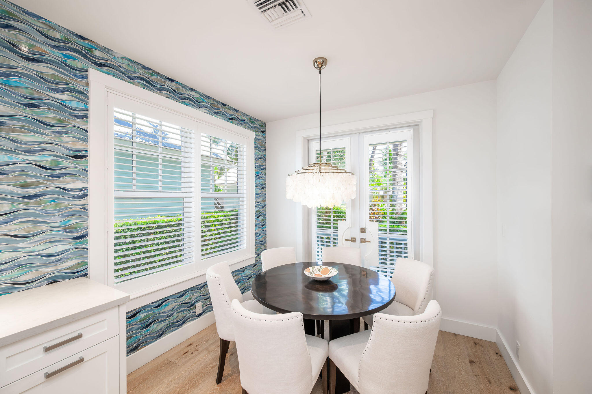 Dining nook with a round table, white chairs, chandelier, and blue wave-patterned wallpaper.