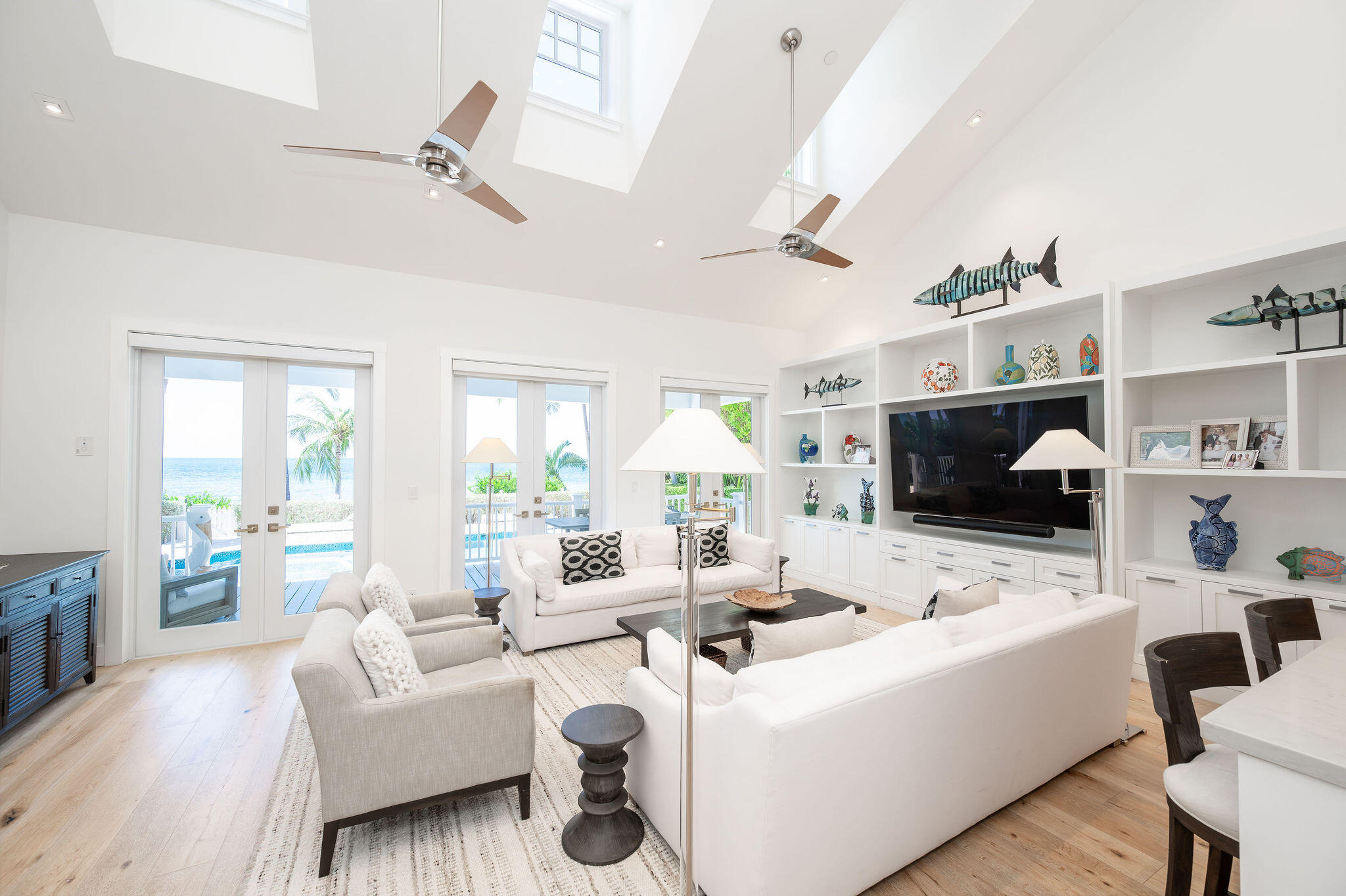 Bright living room with white sofas, skylights, and ocean views through glass doors.