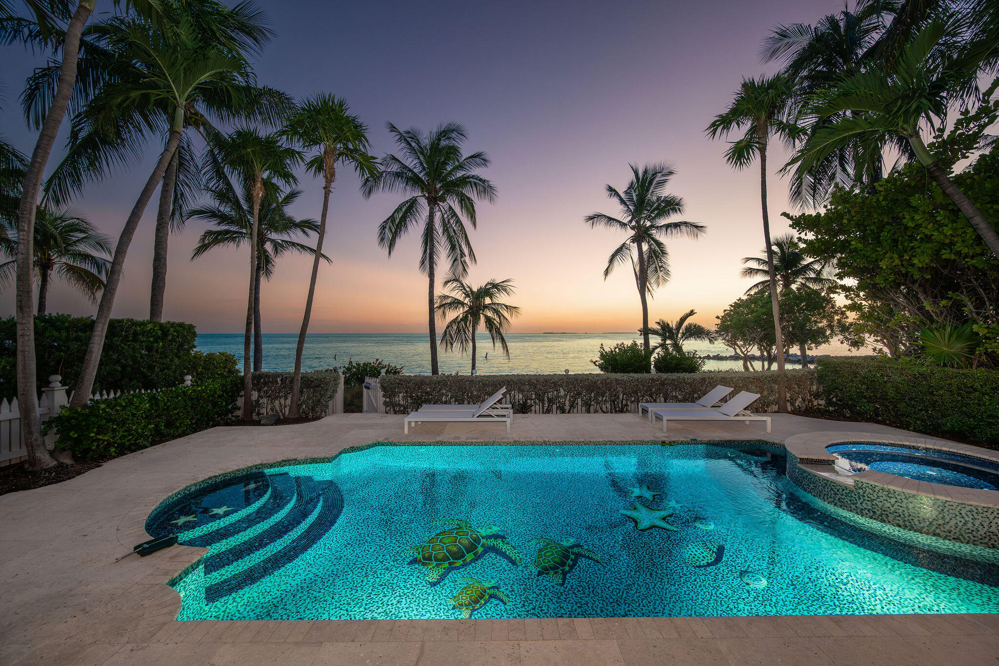 Oceanfront pool and raised spa framed by palm trees at sunset.