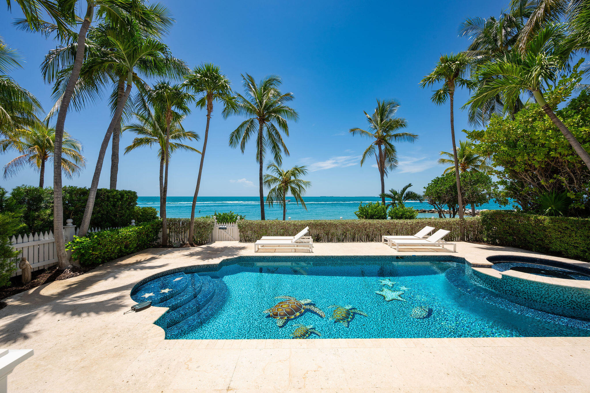 Tropical pool with turtle mosaics, palm trees, and oceanfront views.