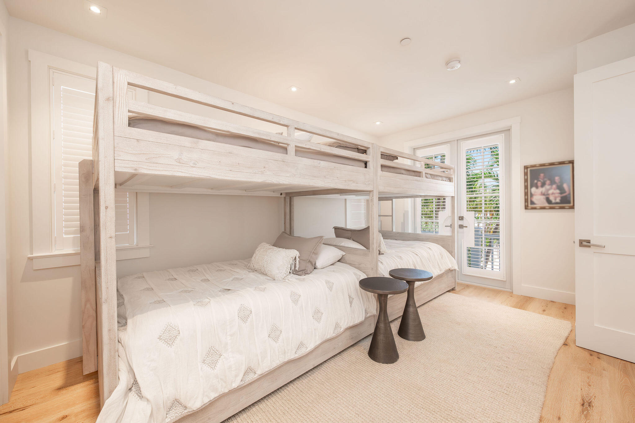 Bedroom with a pale wood bunk bed, white bedding, and plantation-shuttered balcony doors.