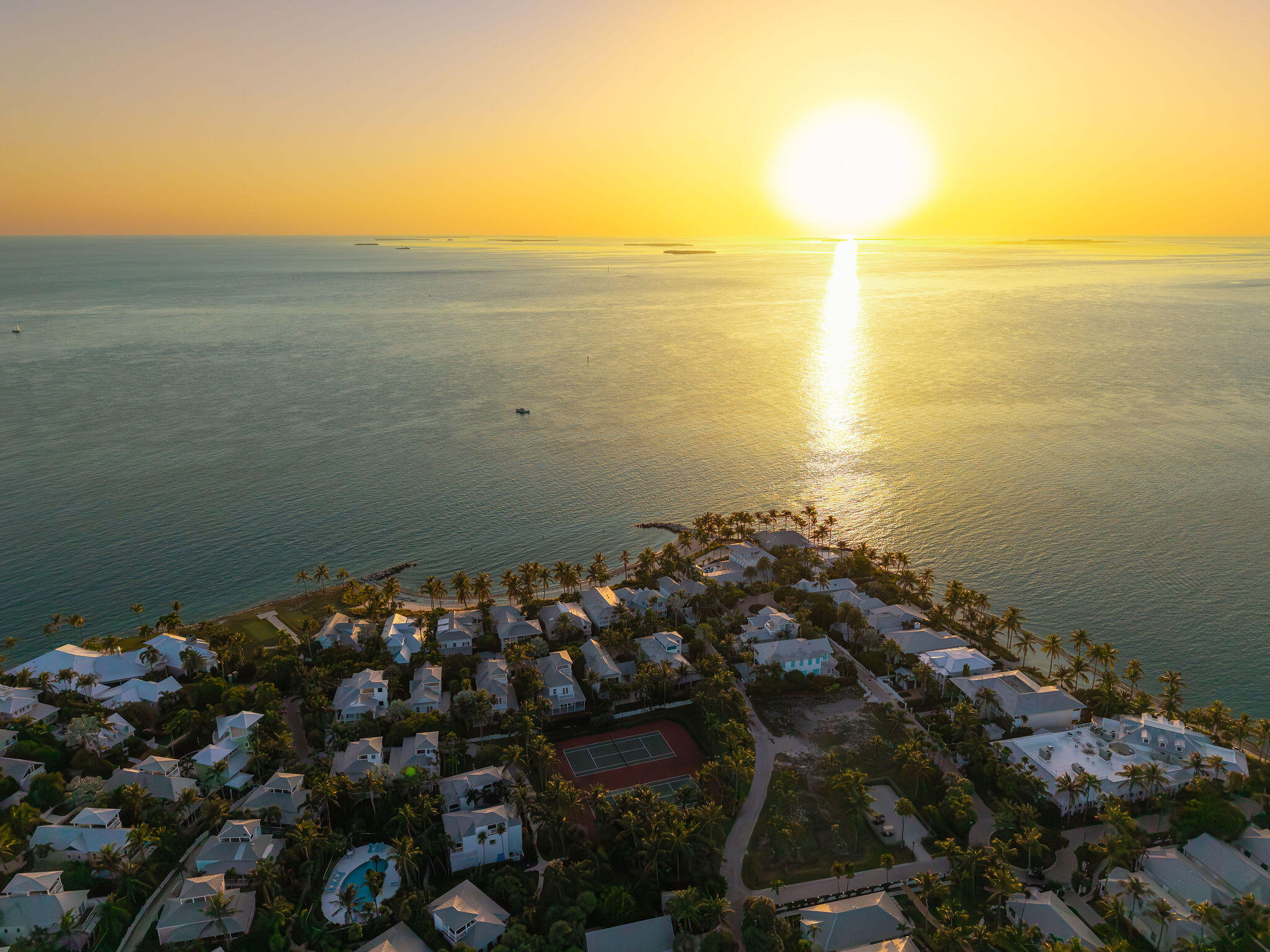 Aerial view of waterfront homes on Sunset Key at sunset, with a tennis court and palm trees.