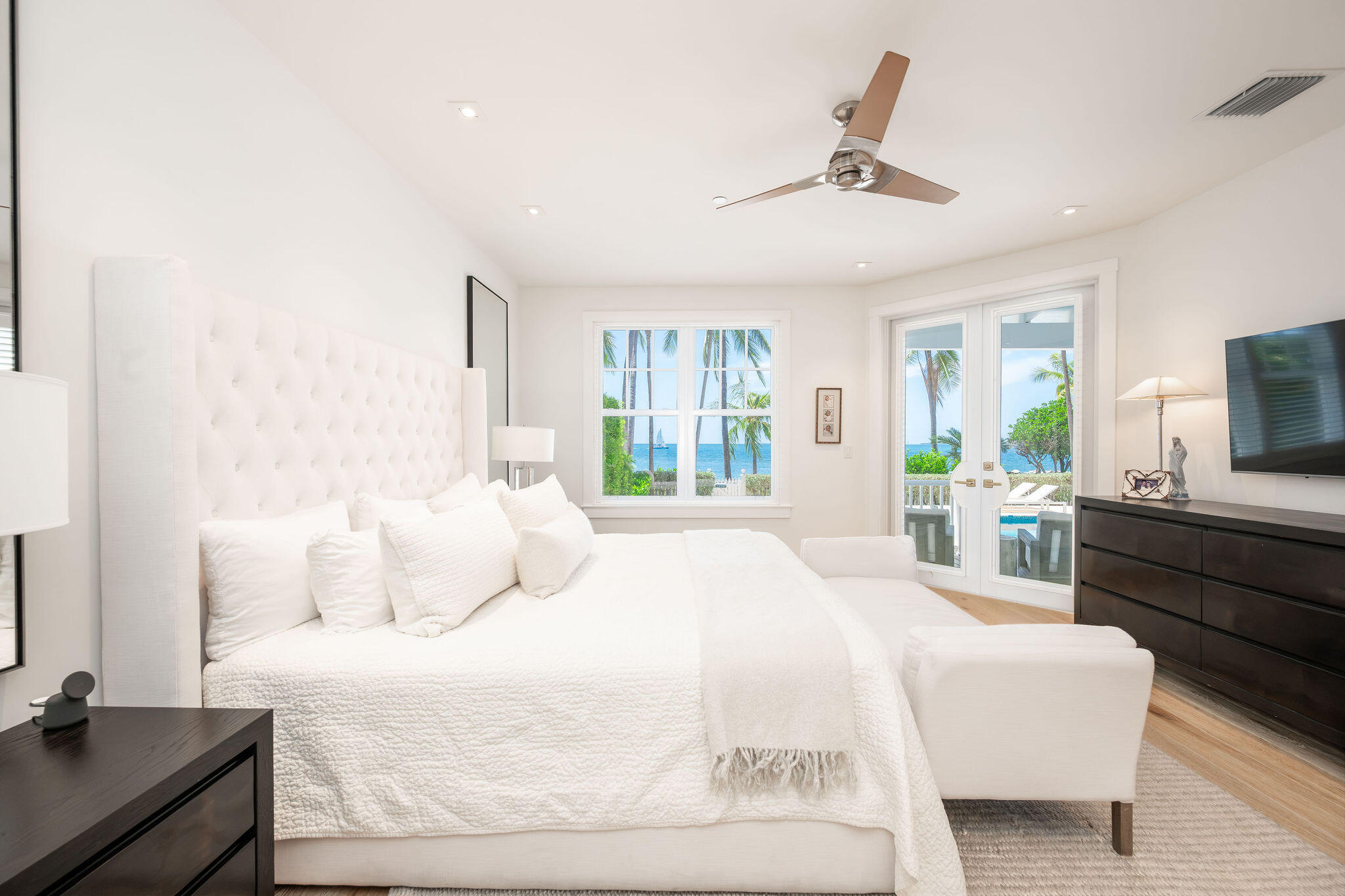 Bright bedroom with a white tufted bed and ocean views through the windows.
