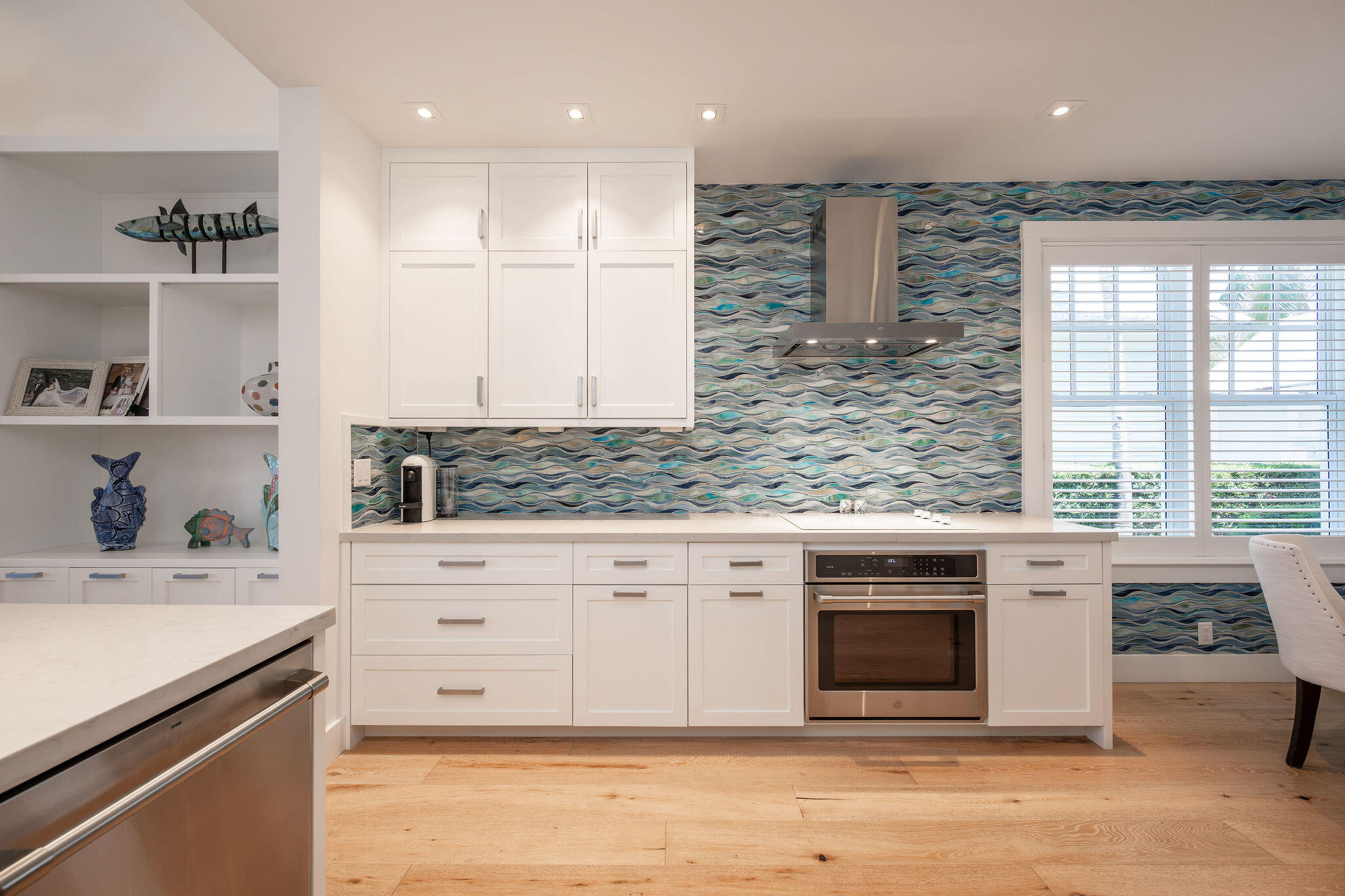 Kitchen with white cabinetry, blue wave-pattern backsplash, stainless steel oven, and fish decor on open shelves.