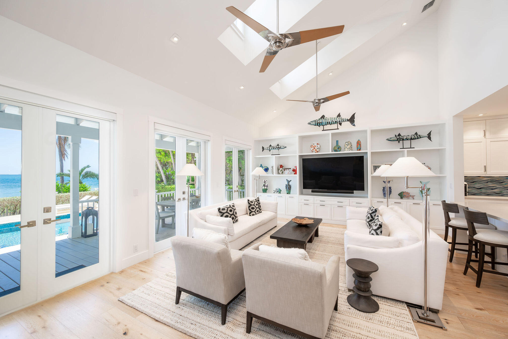 Bright living room with white seating, vaulted ceiling, and ocean views through glass doors.