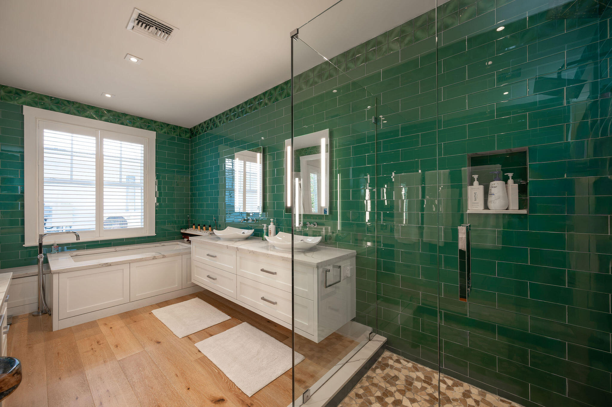 Bathroom with emerald-green tile, a glass shower, double vanity, and built-in soaking tub.