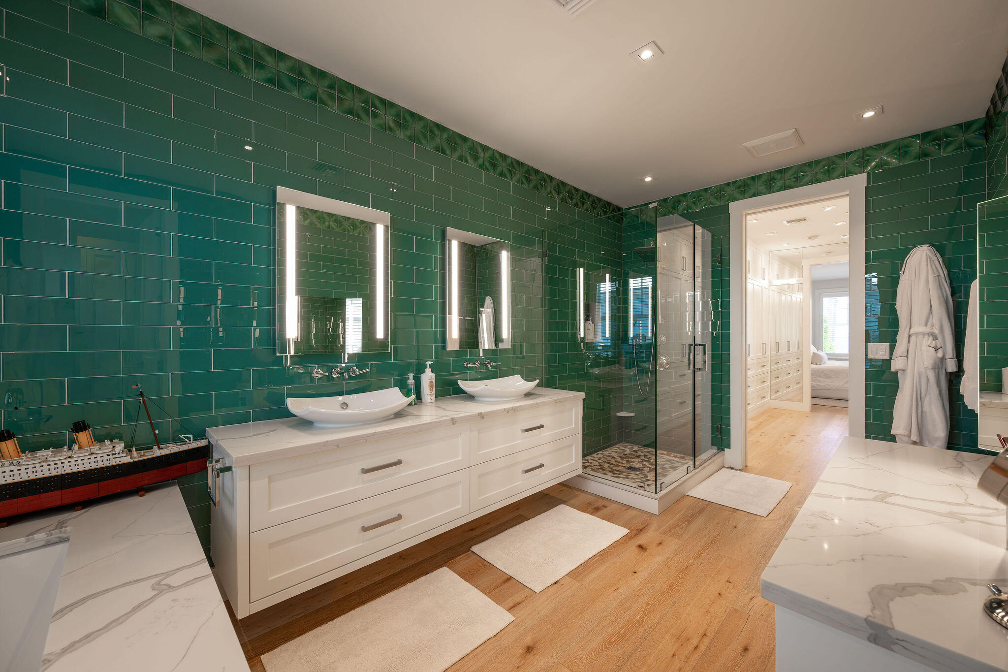 Bathroom with emerald-green tile, a double vanity, and a glass-enclosed shower.