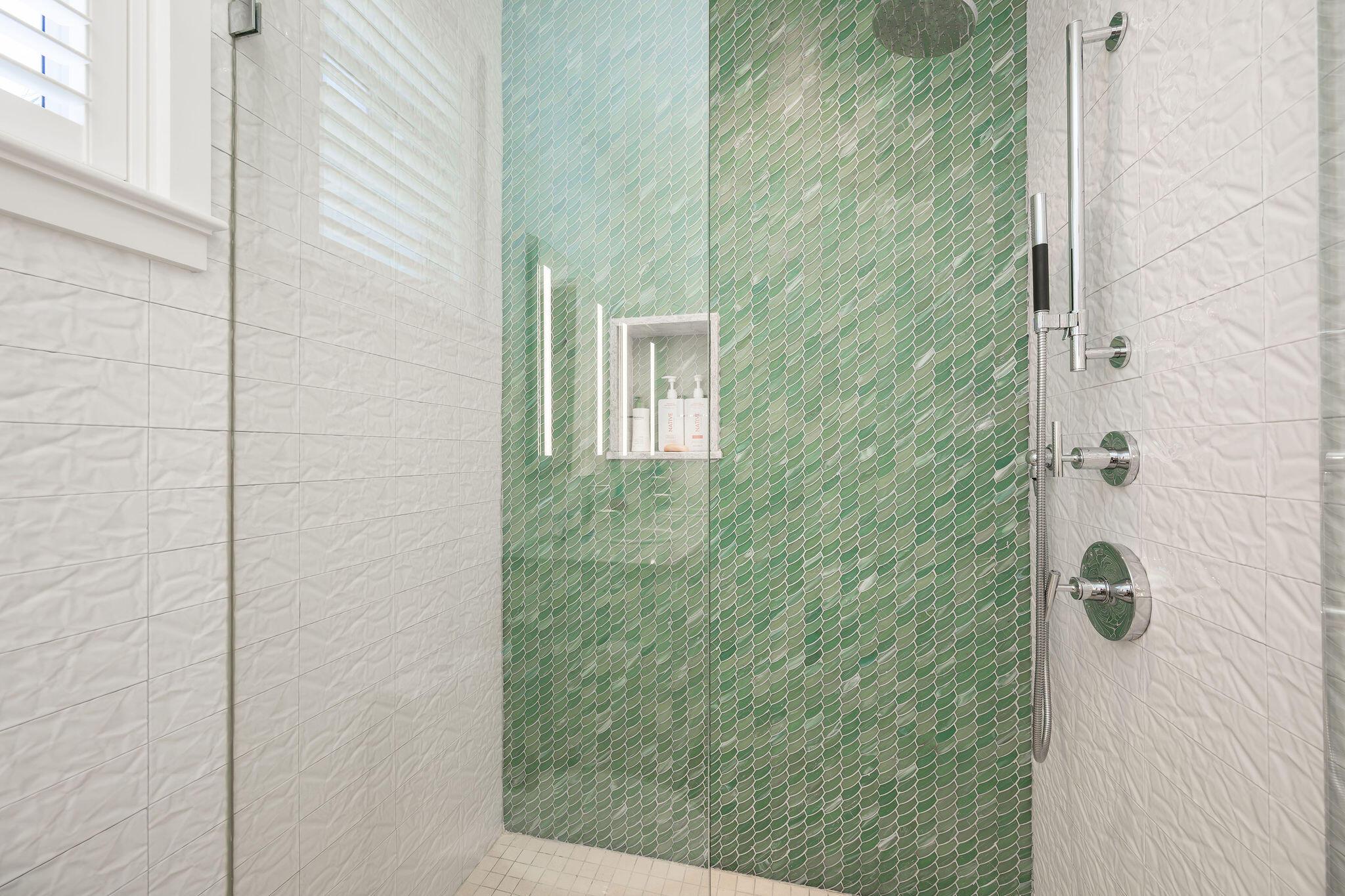 Bathroom shower with a green scallop-tile accent wall, chrome fixtures, and recessed toiletry niche.