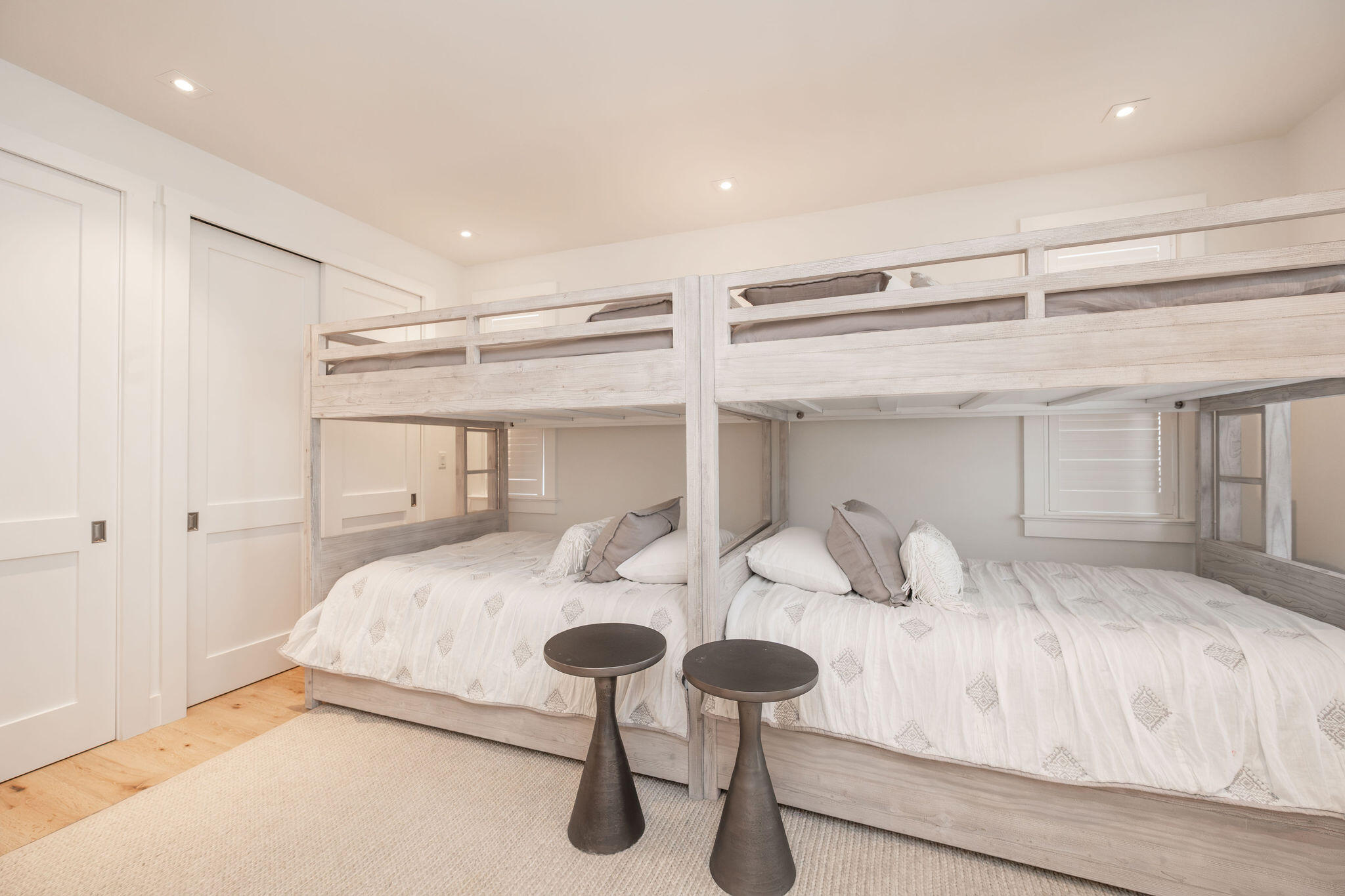Bedroom with a whitewashed bunk-bed structure, patterned white bedding, and two dark pedestal tables.