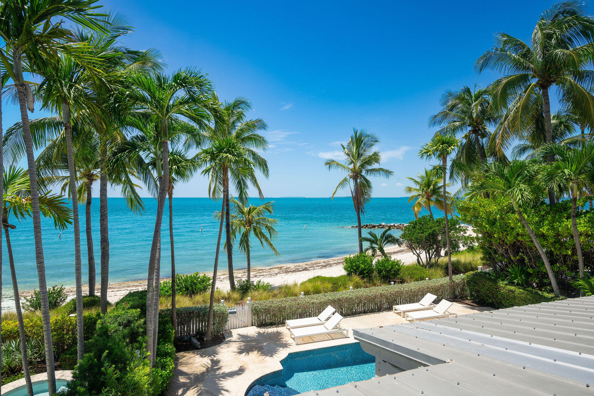 Beachfront pool and lounge chairs overlook a palm-lined sandy beach and turquoise ocean.