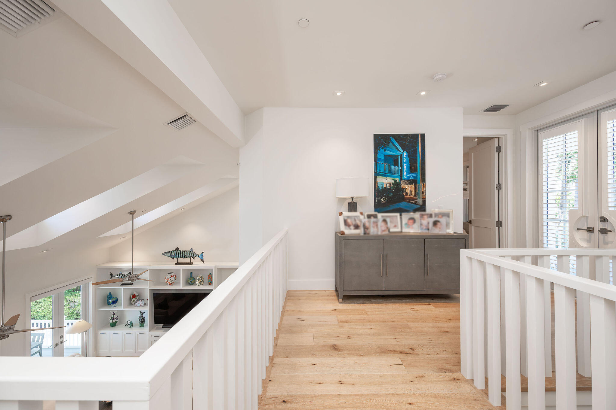 Upstairs landing with light wood floors, white railings, and a gray console cabinet.