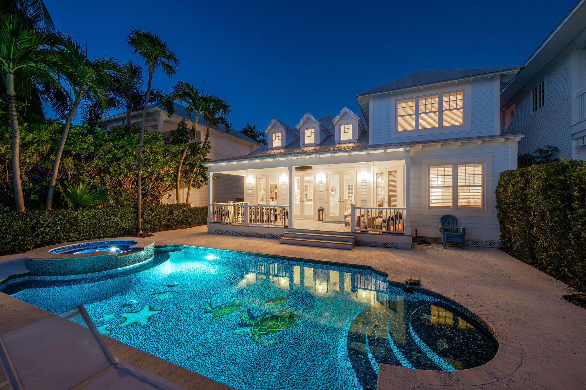 White coastal home with a glowing pool, raised spa, and sea turtle mosaics at night.