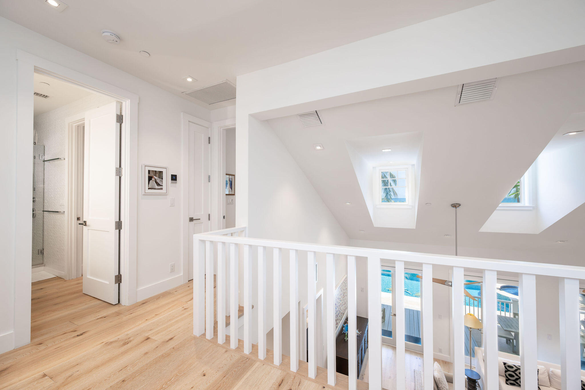 Upstairs landing with a white railing, vaulted skylight ceiling, and pool visible below.