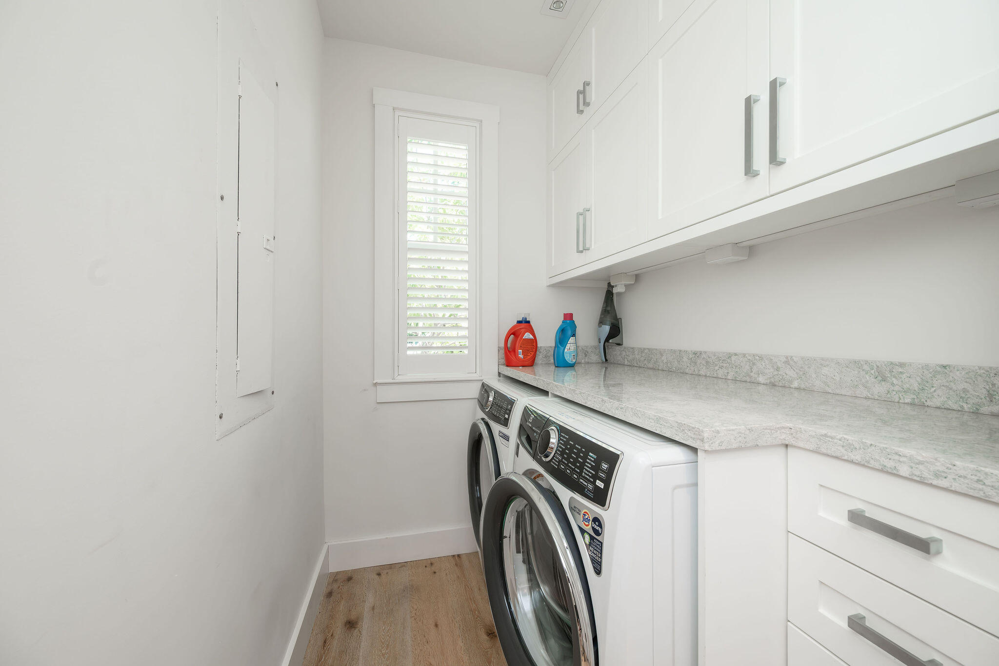 Laundry room with front-loading washer and dryer, white cabinets, and a shuttered window.