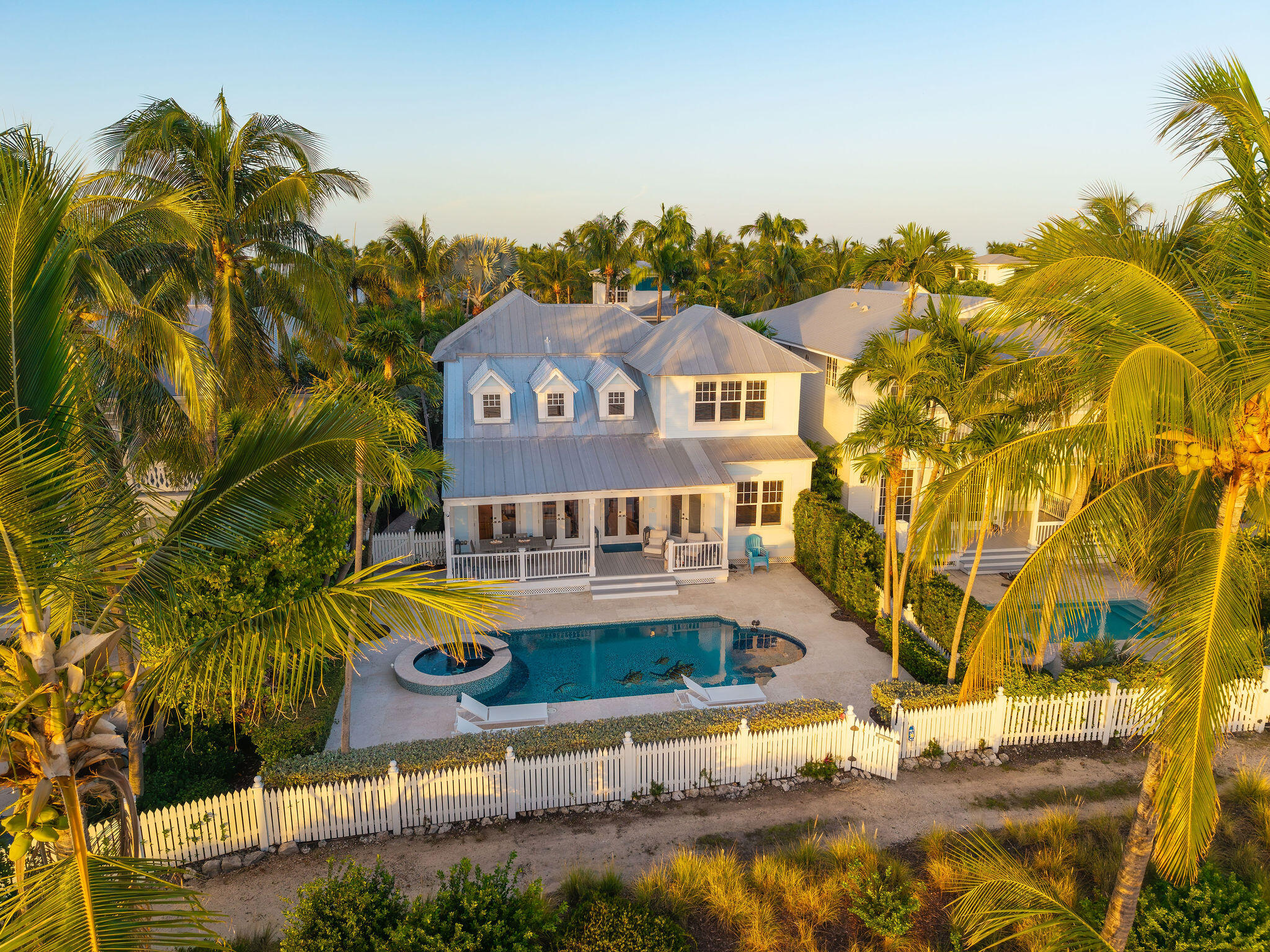 Aerial view of a white Key West home and pool, framed by palms and a white picket fence.