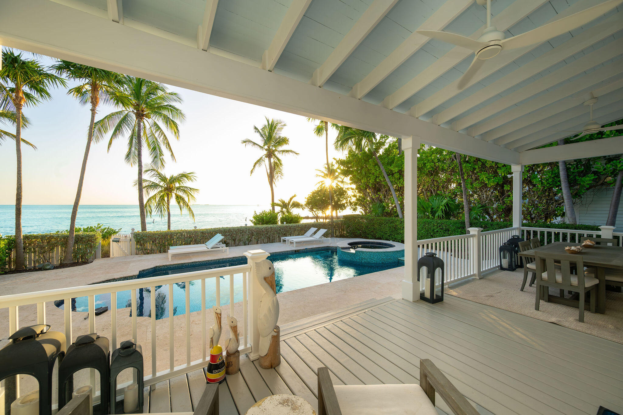 Covered waterfront patio overlooking a pool and spa, with palm trees and ocean beyond.
