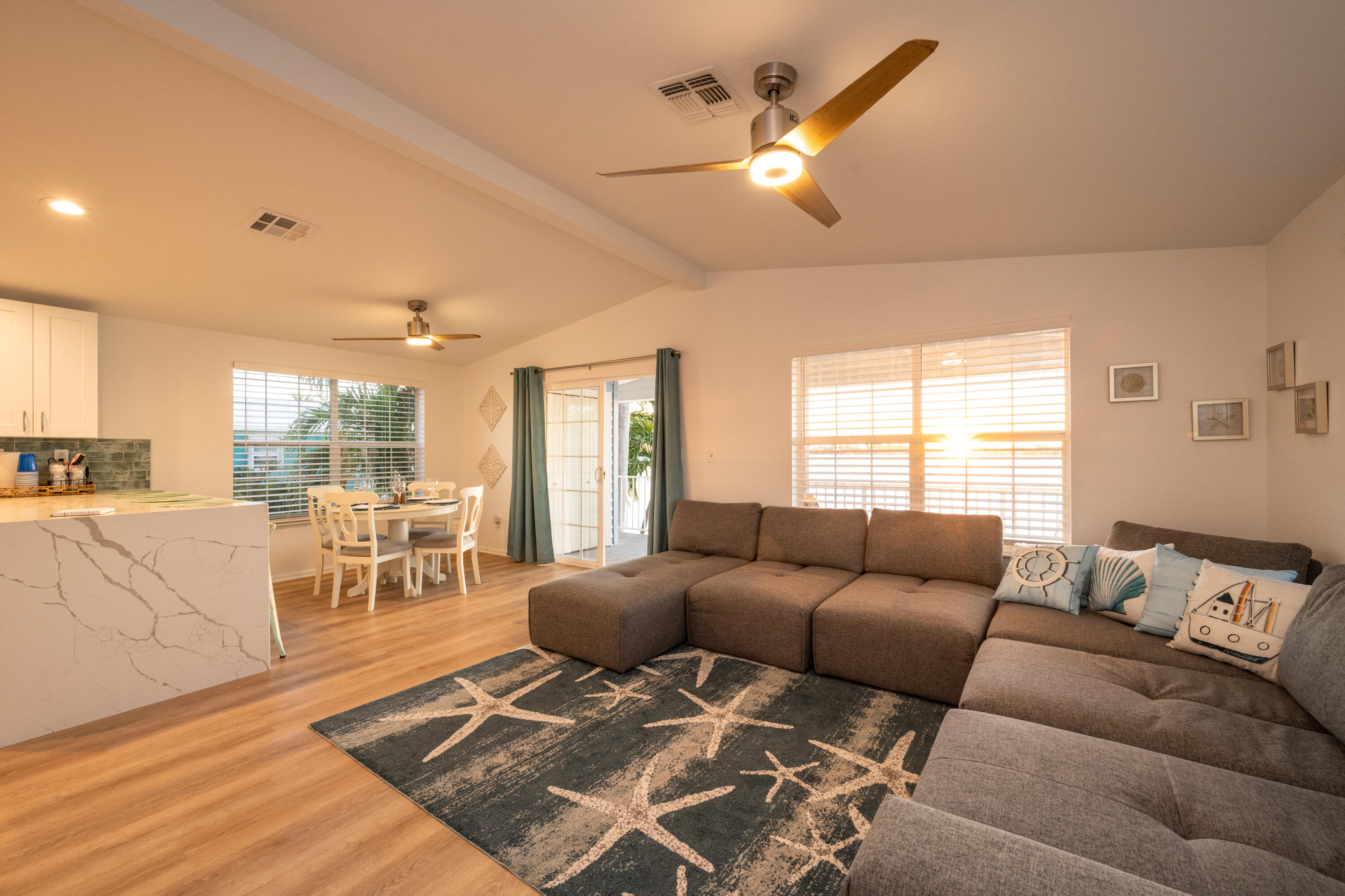 Living room with a large gray sectional, starfish-patterned rug, and open dining area beside the kitchen.