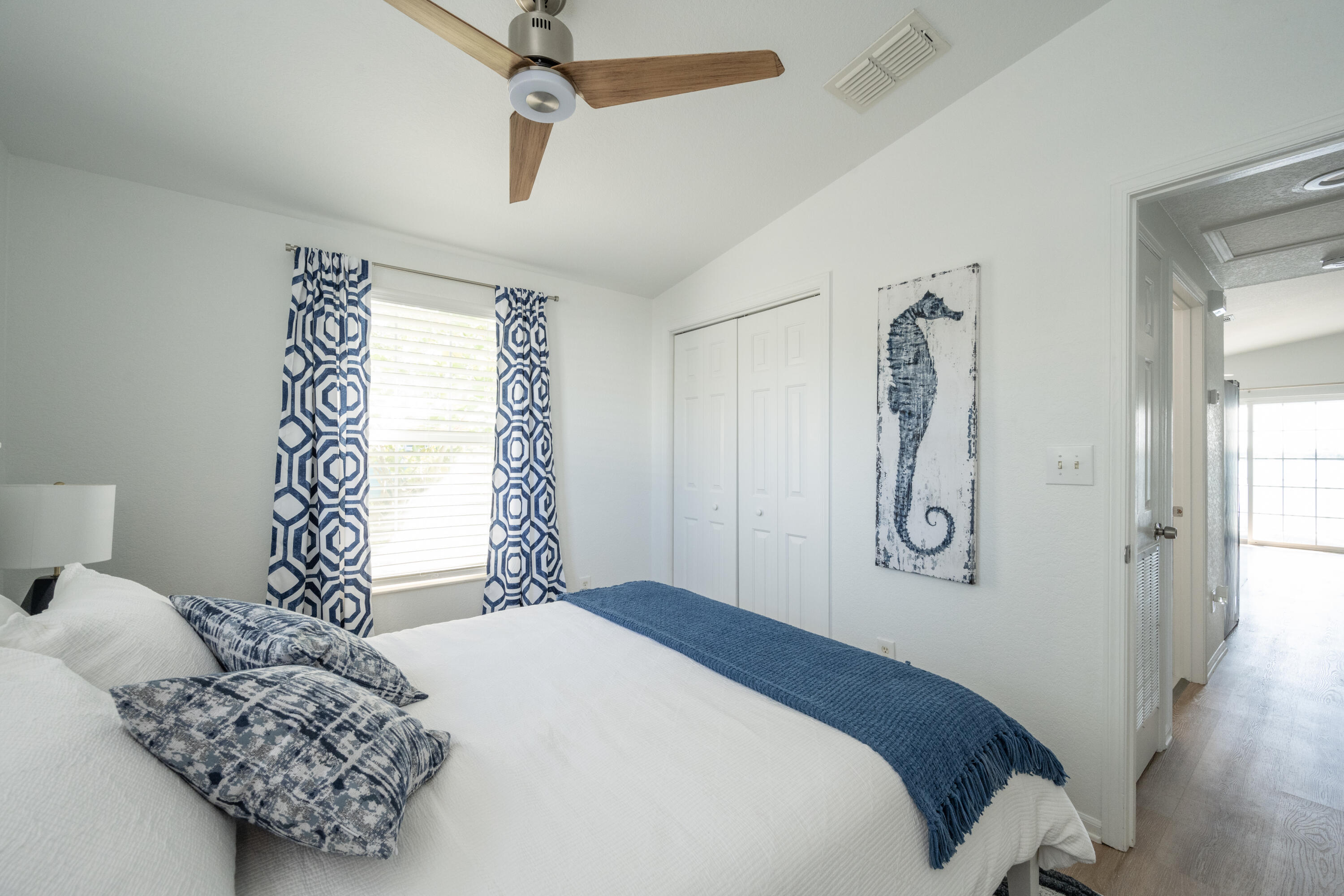 Bedroom with a white bed, blue accents, patterned curtains, and seahorse wall art.