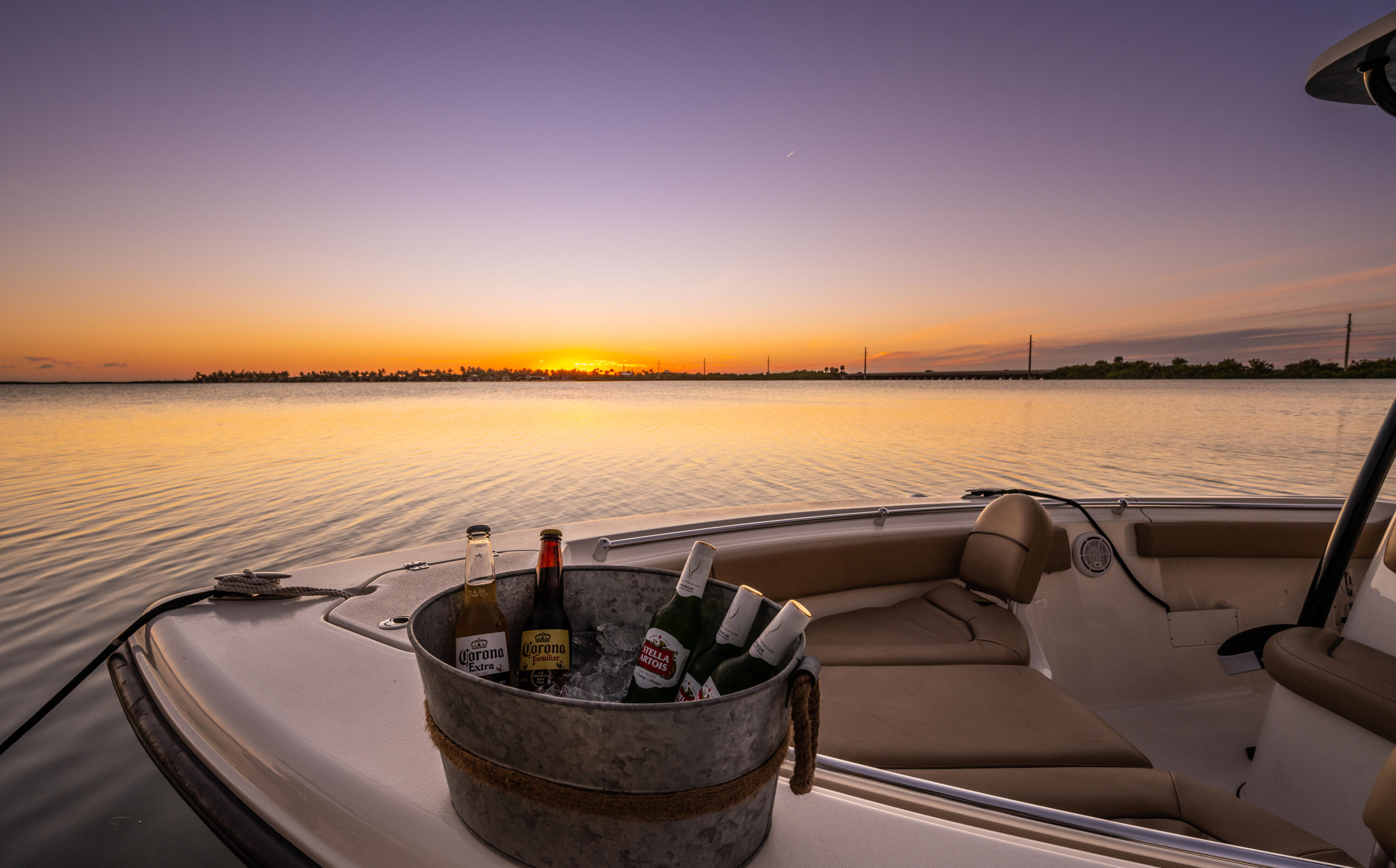 Motorboat seating and an ice bucket of drinks overlook calm water at sunset.