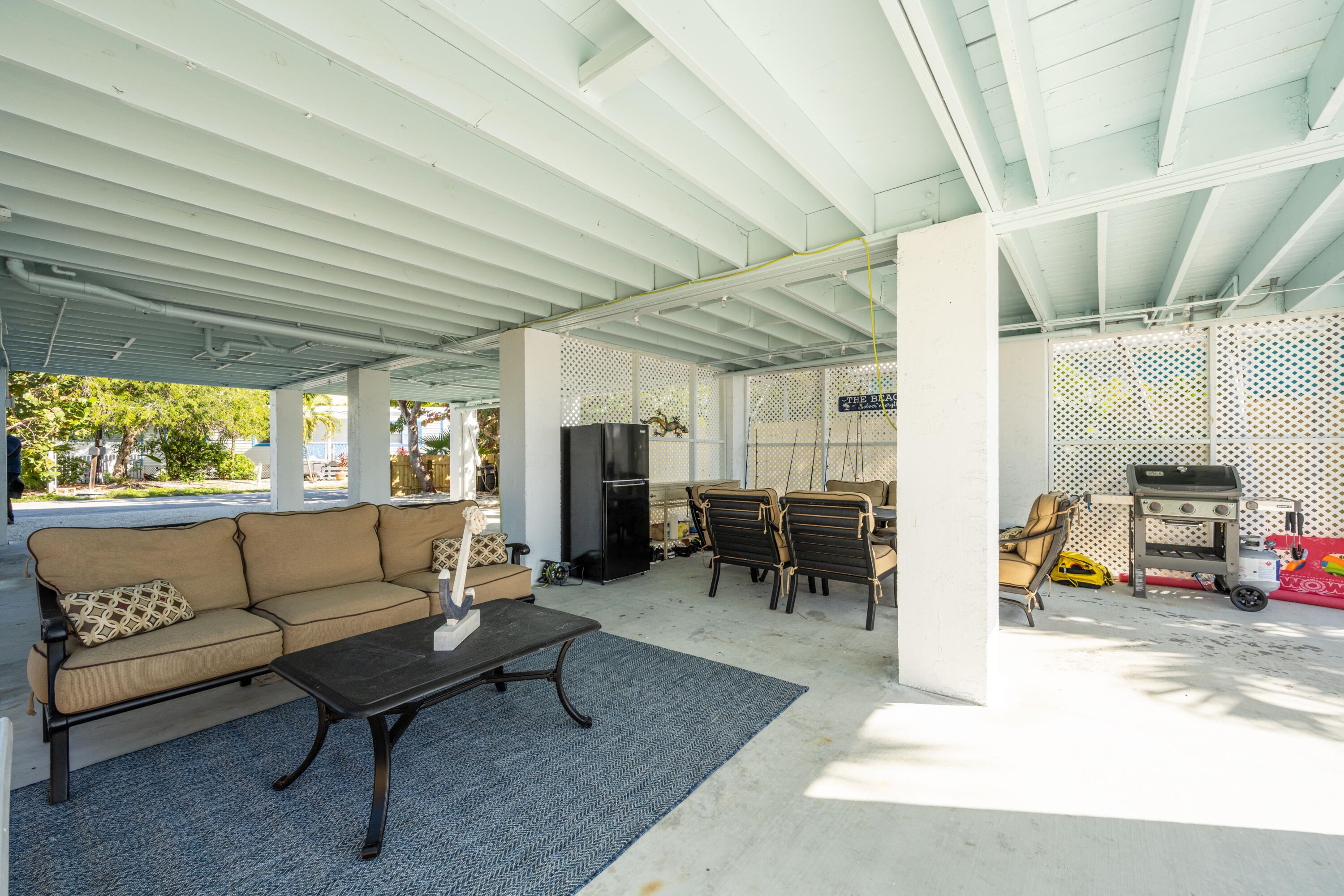 Covered patio with tan seating, a blue rug, dining chairs, and a barbecue grill.