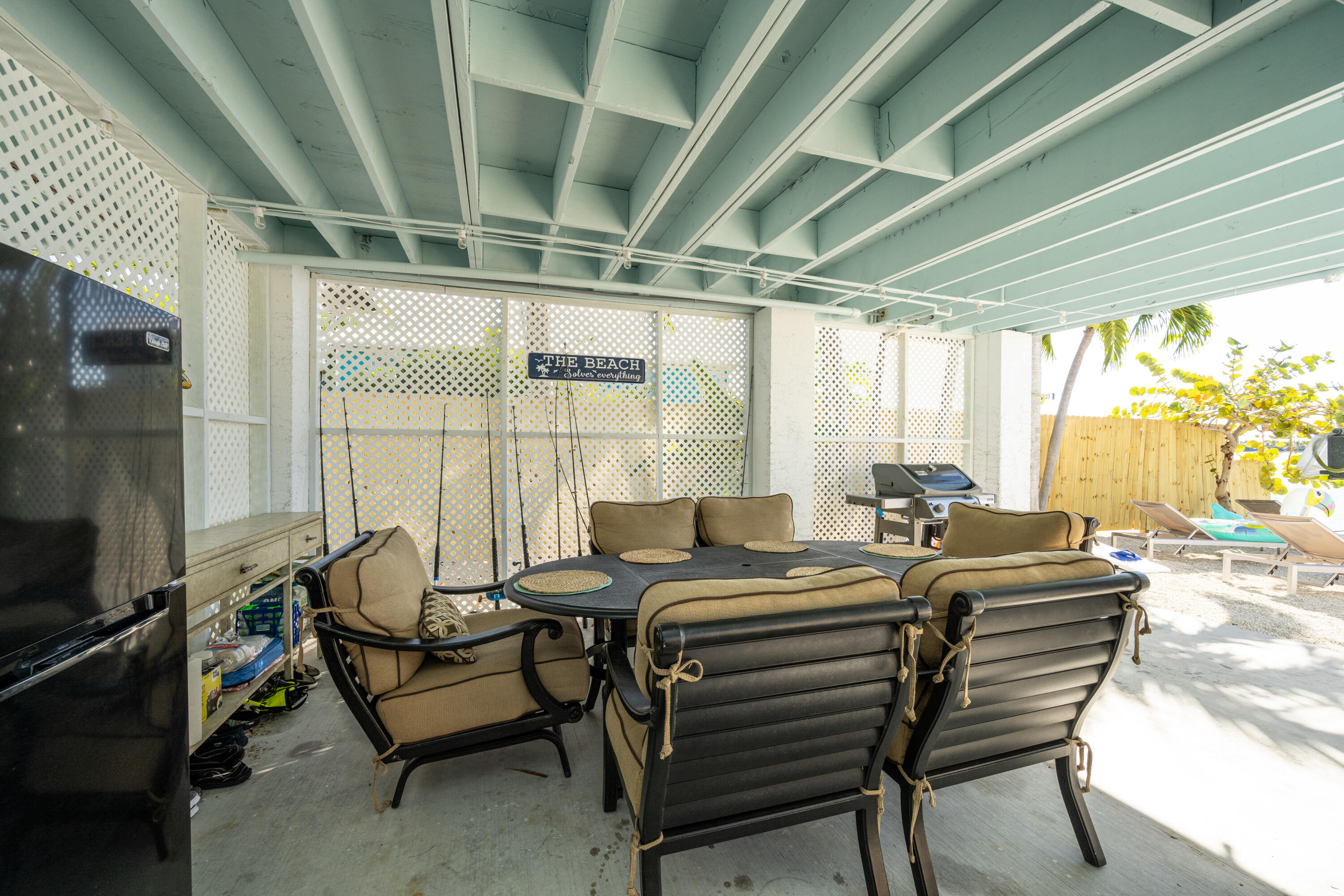 Covered patio with cushioned seating, a dining table, and a barbecue grill opening onto a sunny yard.