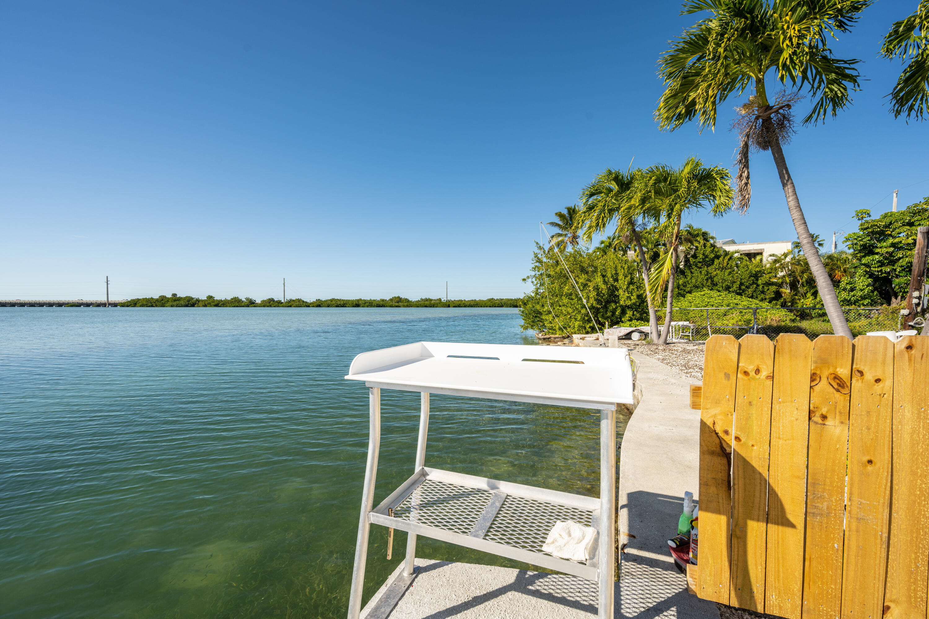 Waterfront dock with a white fish-cleaning station, wooden fence, and palm trees.