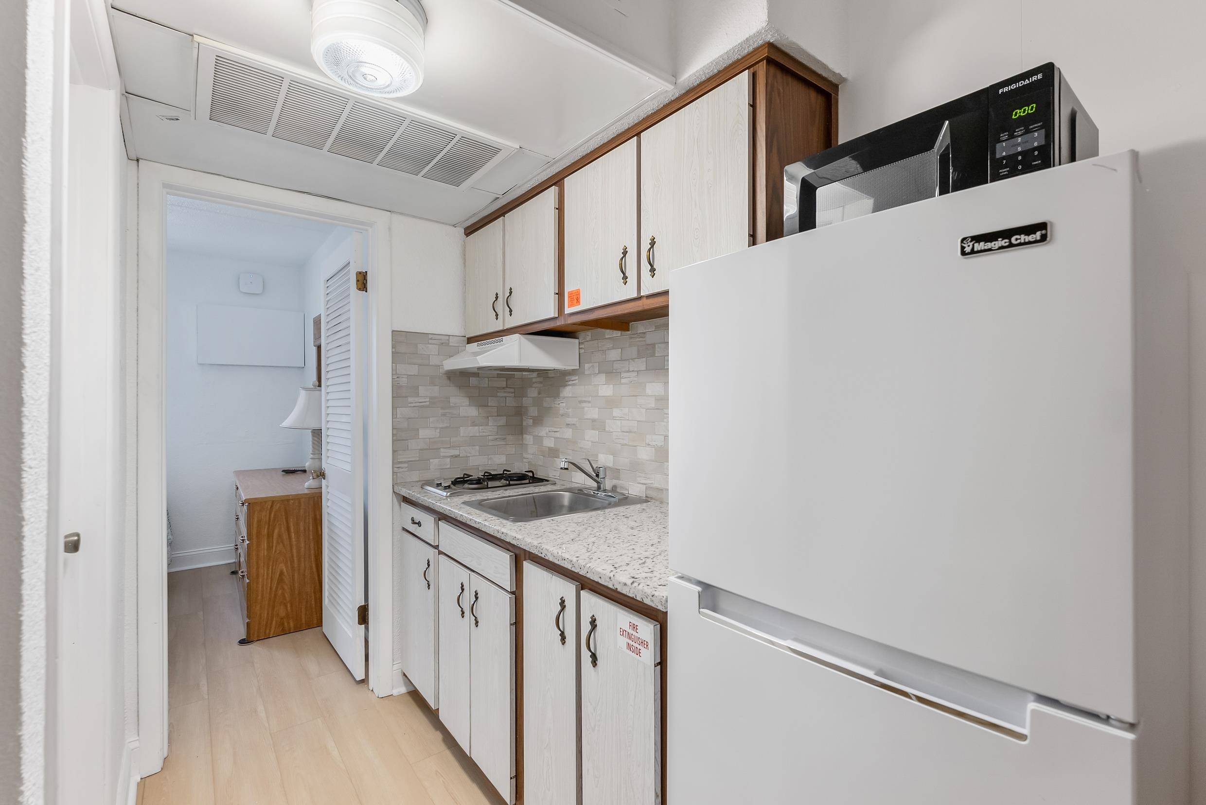 Compact kitchen with a large white refrigerator, gas cooktop, and tiled backsplash.