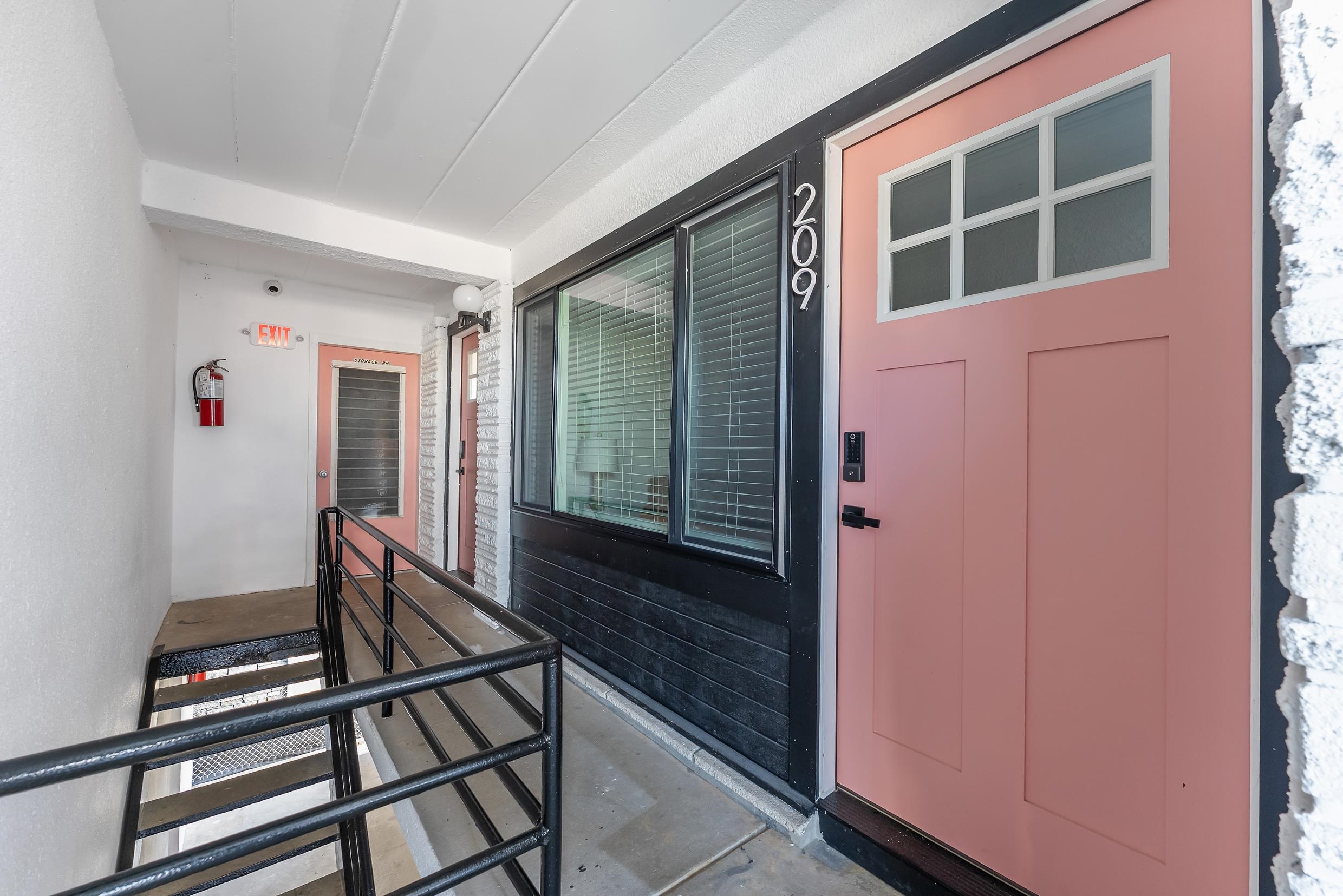 Unit 209’s salmon-pink entry door and window along an exterior walkway.