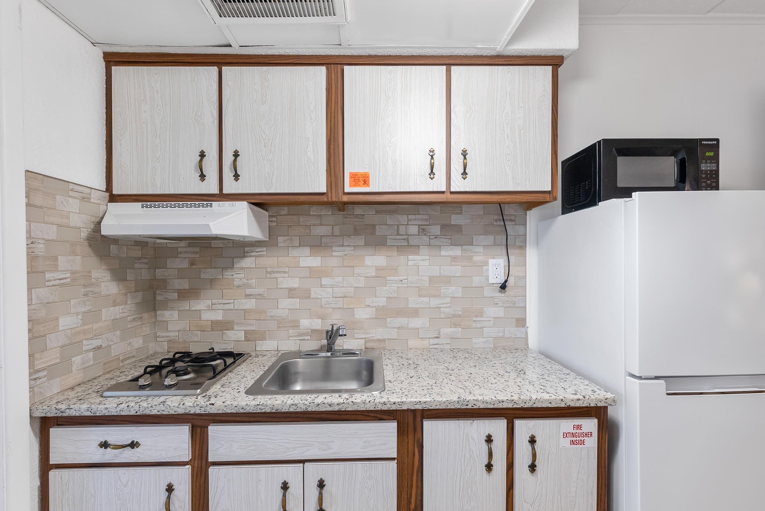 Compact kitchen with a gas cooktop, stainless sink, tiled backsplash, and white woodgrain cabinets.