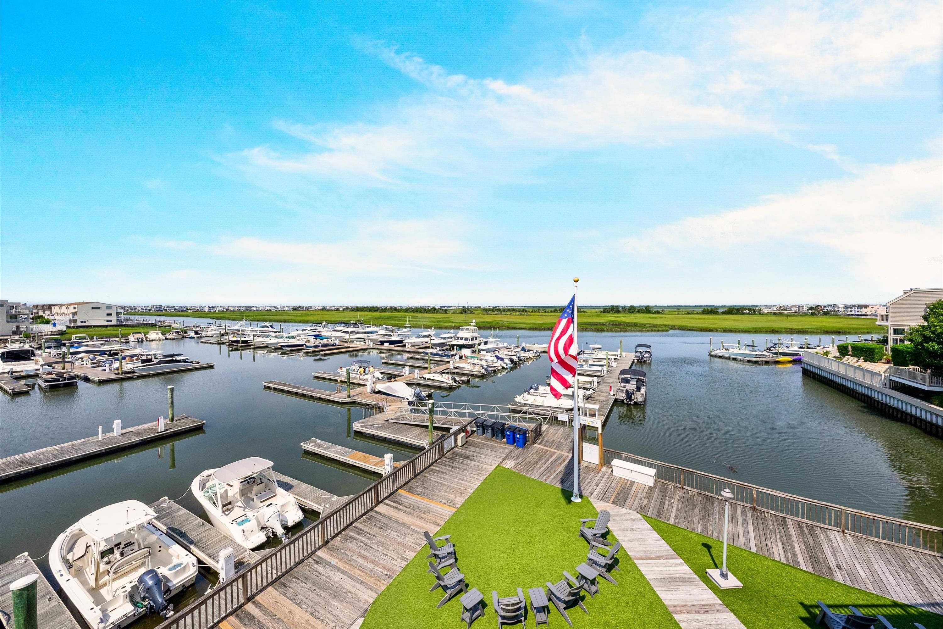 Marina with boats and docks viewed from a waterfront deck with turf and Adirondack chairs.