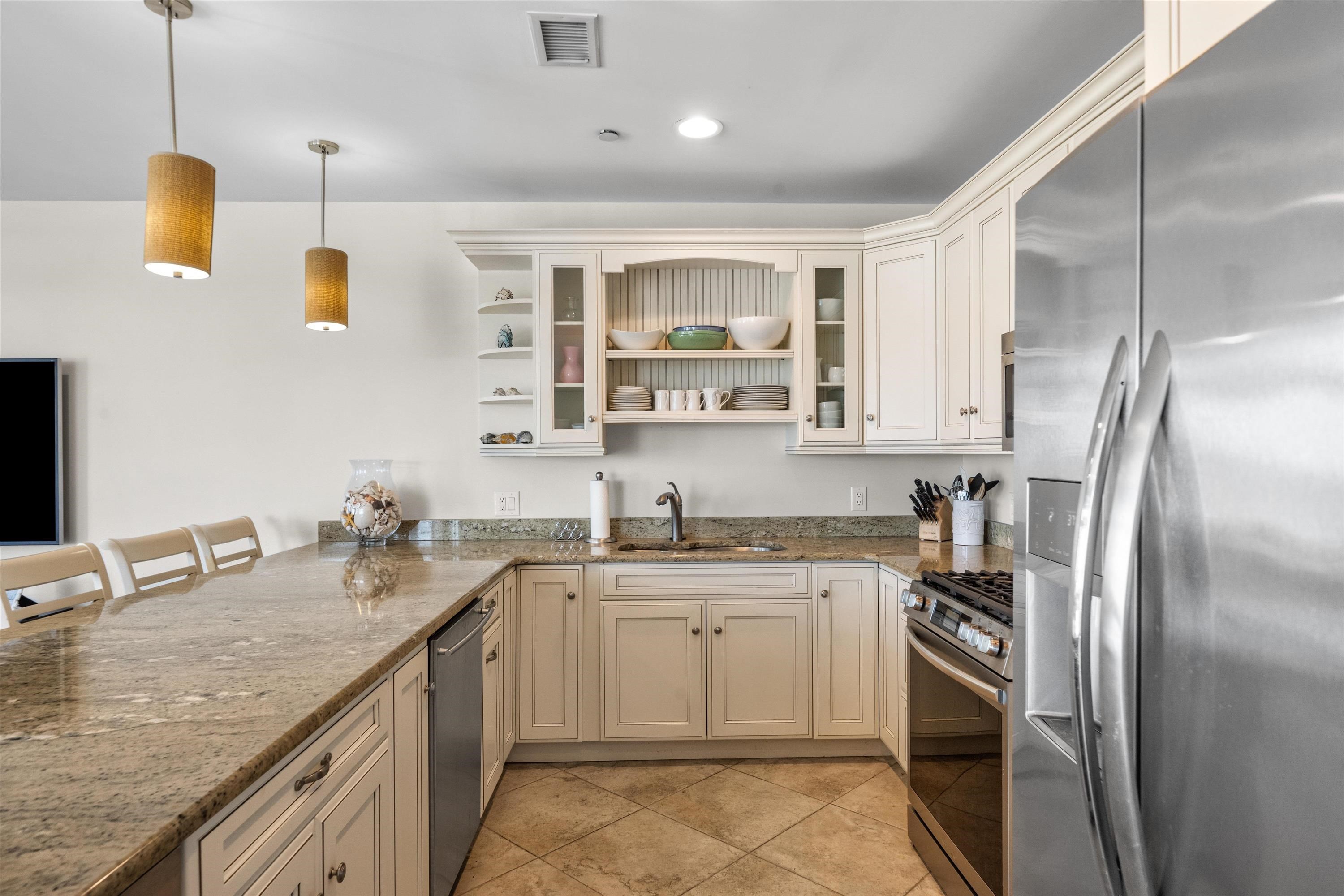 Kitchen with cream cabinets, granite counters, stainless steel appliances, and woven pendant lights.