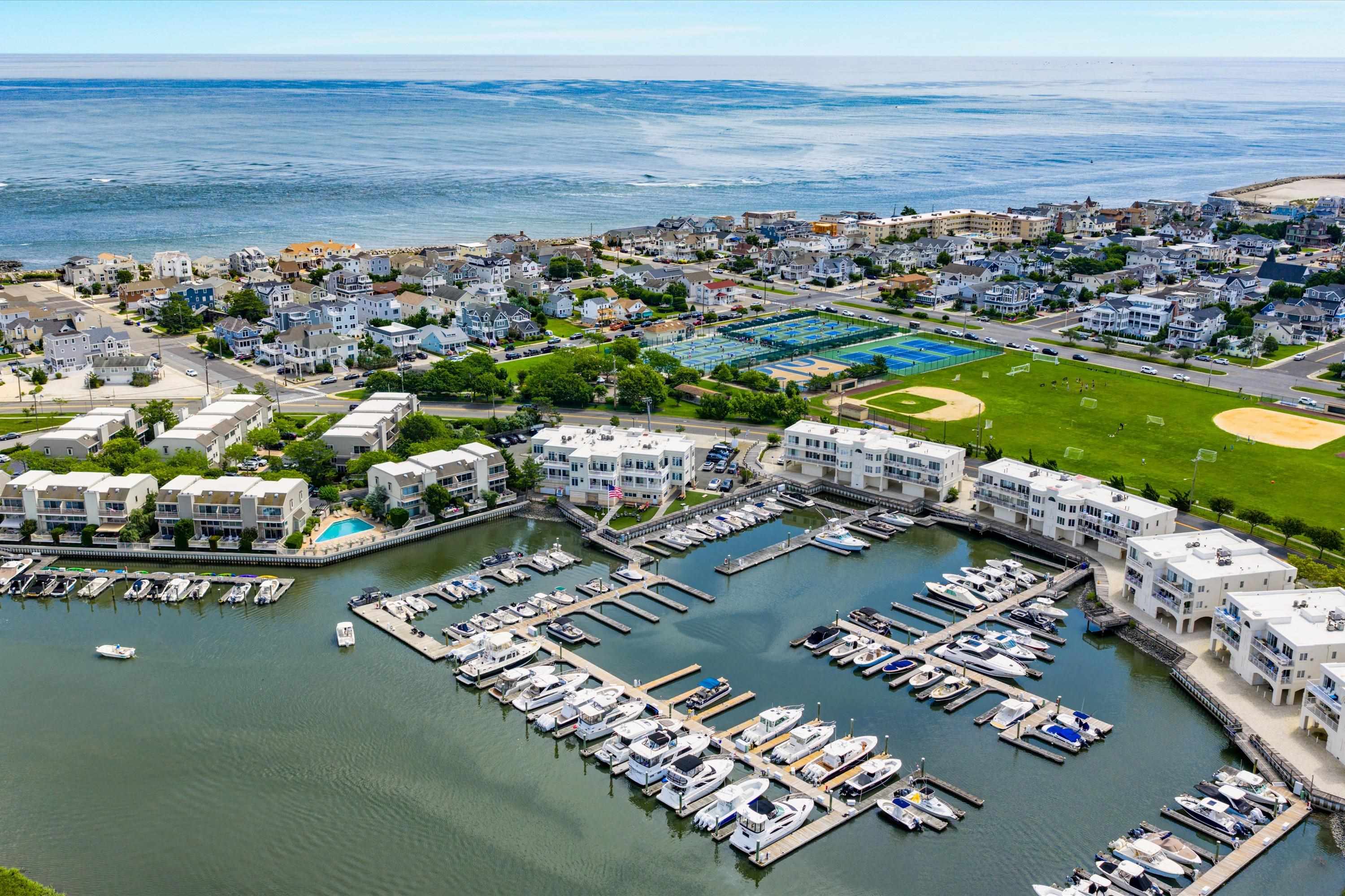 Aerial view of a waterfront marina with boats, condominiums, tennis courts, and oceanfront homes.