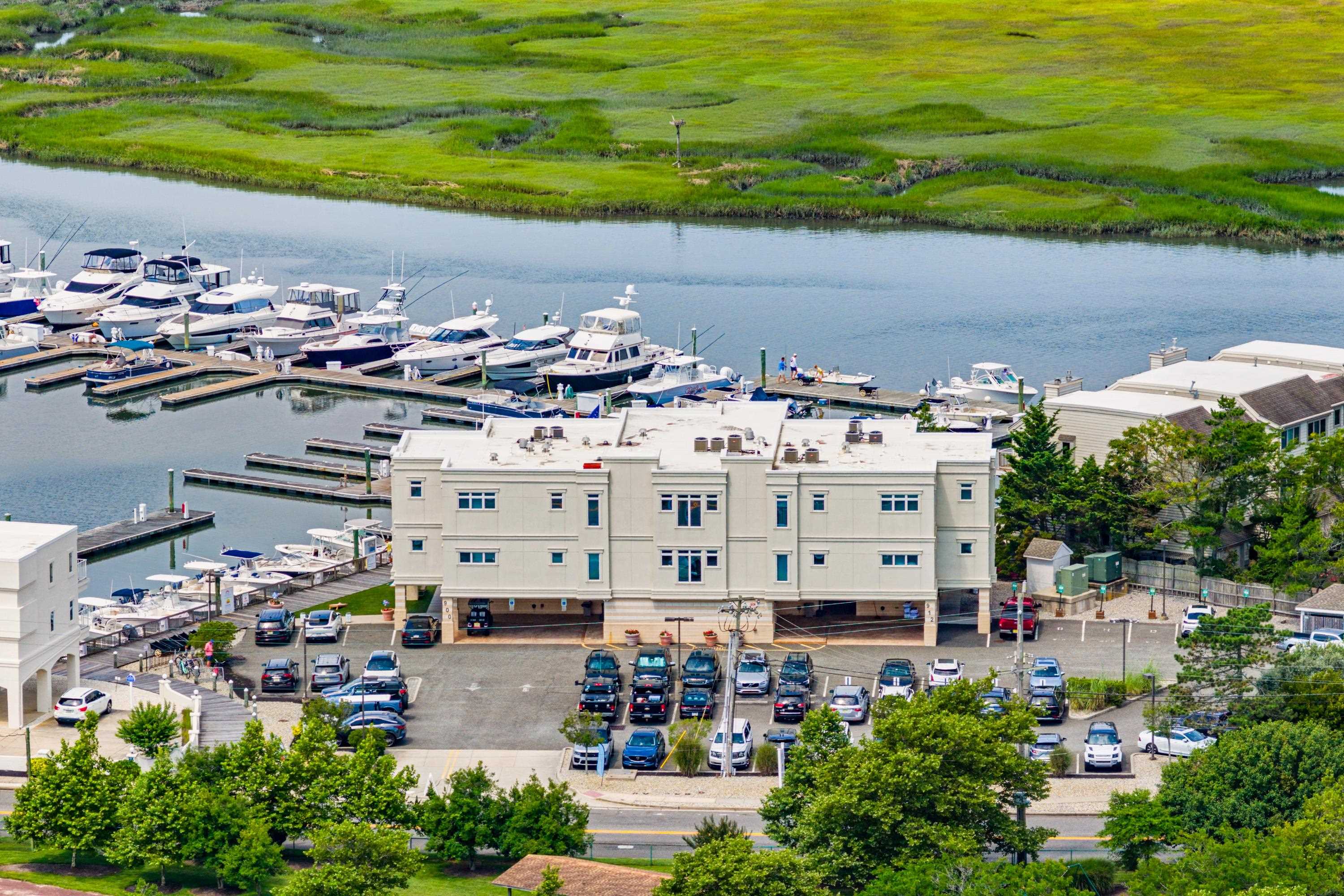 Waterfront building beside a marina, with docked boats and green marshland across the water.