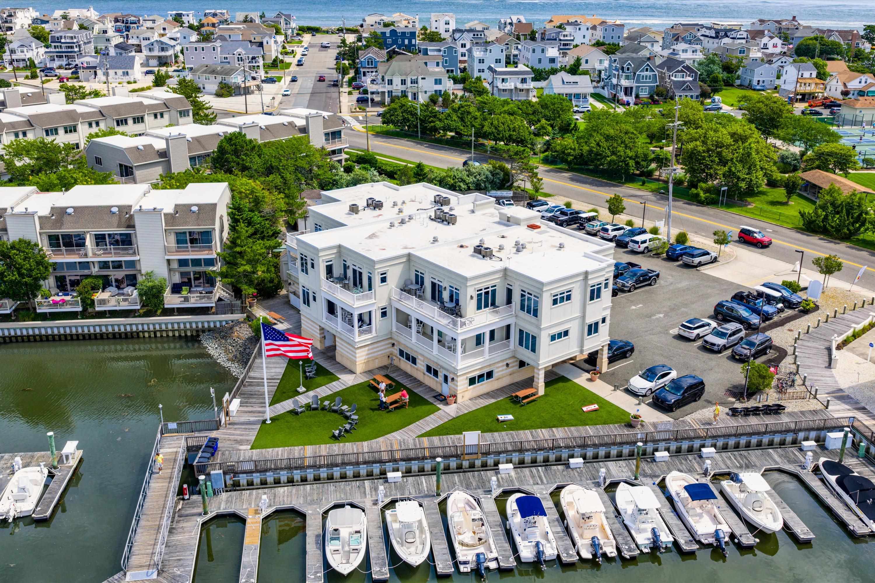 Aerial view of a waterfront condominium beside a marina, with boats, boardwalk, and landscaped lawn.