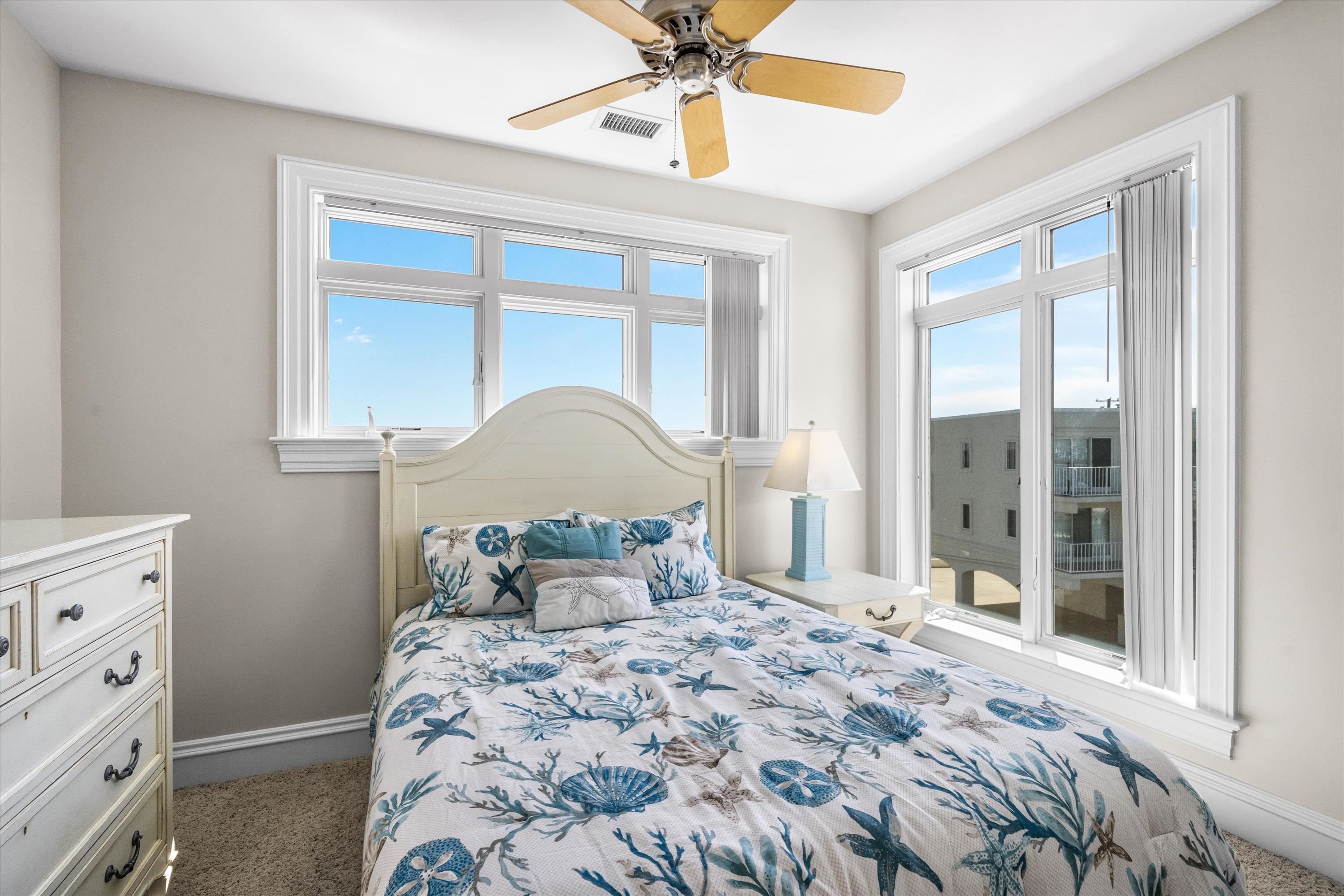 Bedroom with blue marine-patterned bedding and large windows overlooking a neighboring building.