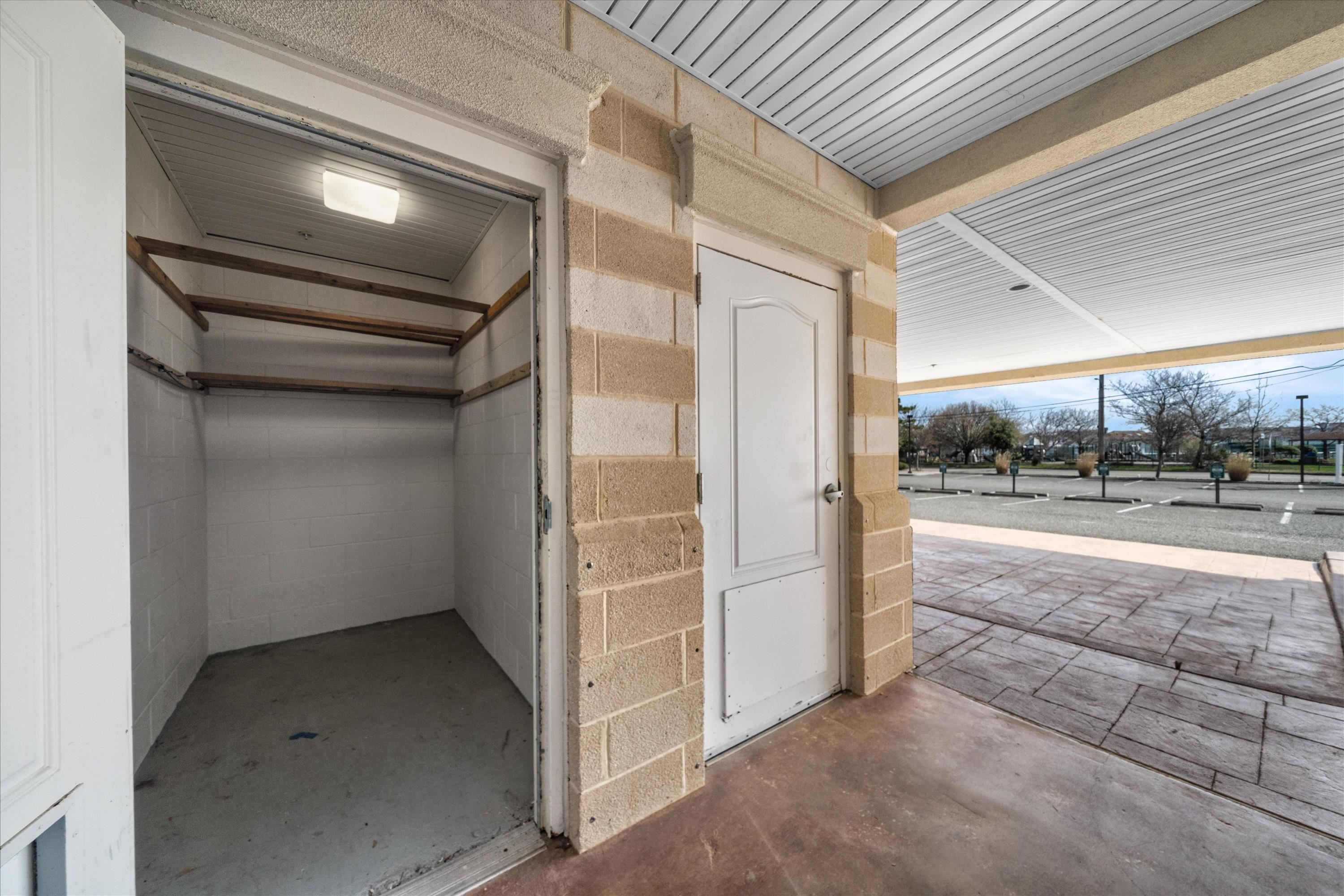Empty storage garage with wooden shelves beside a covered paved area and parking lot.