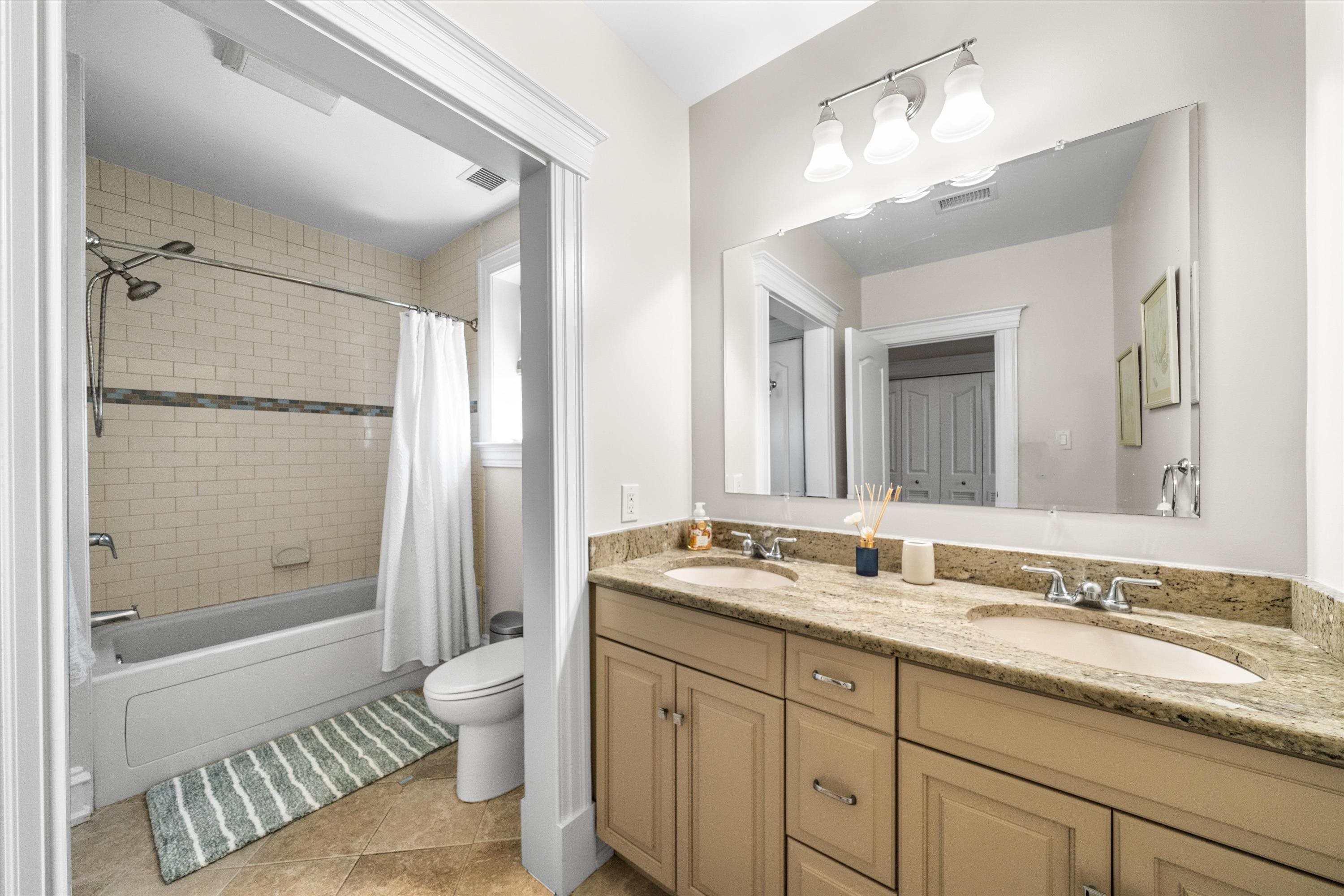 Bathroom with a double-sink granite vanity and a subway-tile tub and shower.