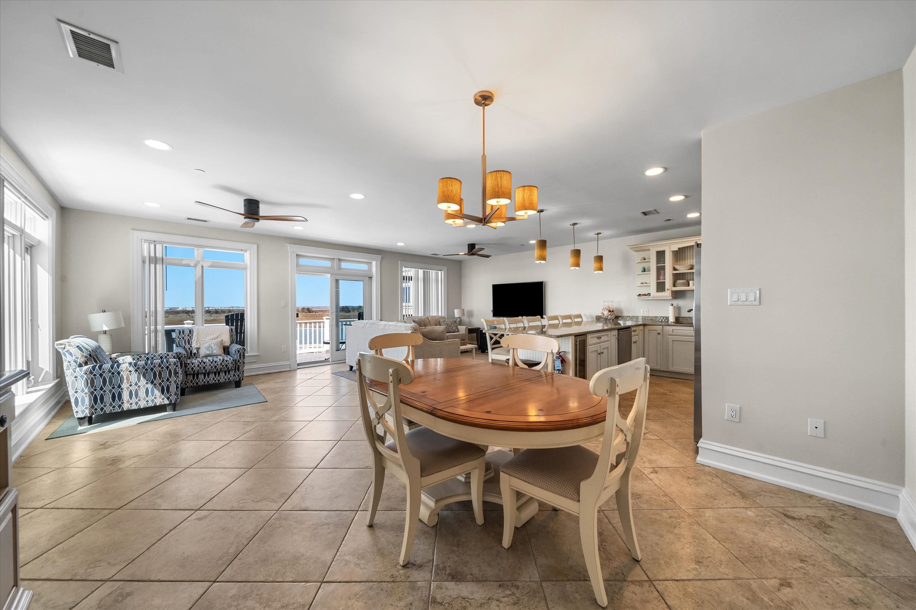 Open-plan dining and living area with a wood table, kitchen island, and large windows.