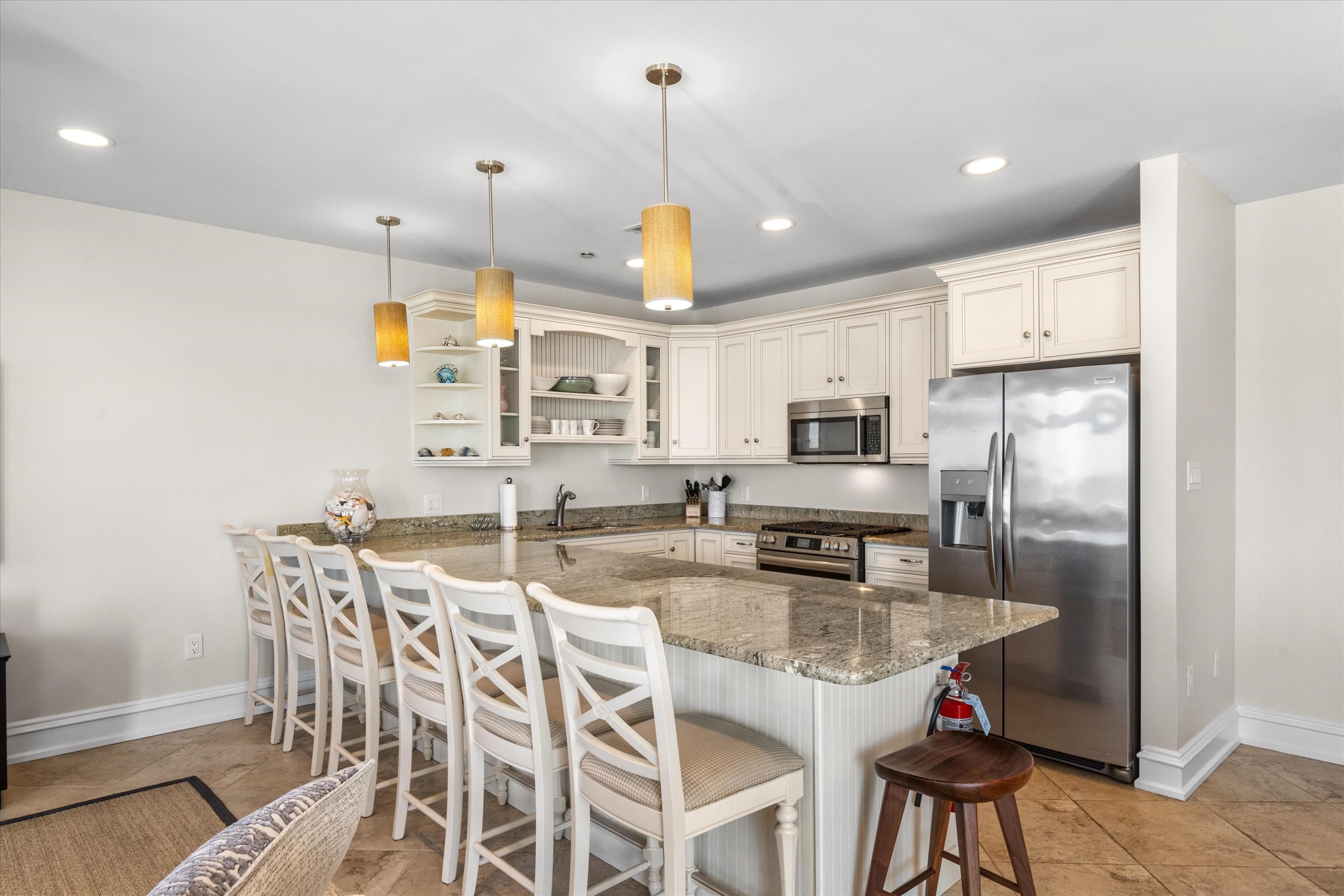 Kitchen with white cabinetry, granite island and bar stools, and stainless steel appliances.