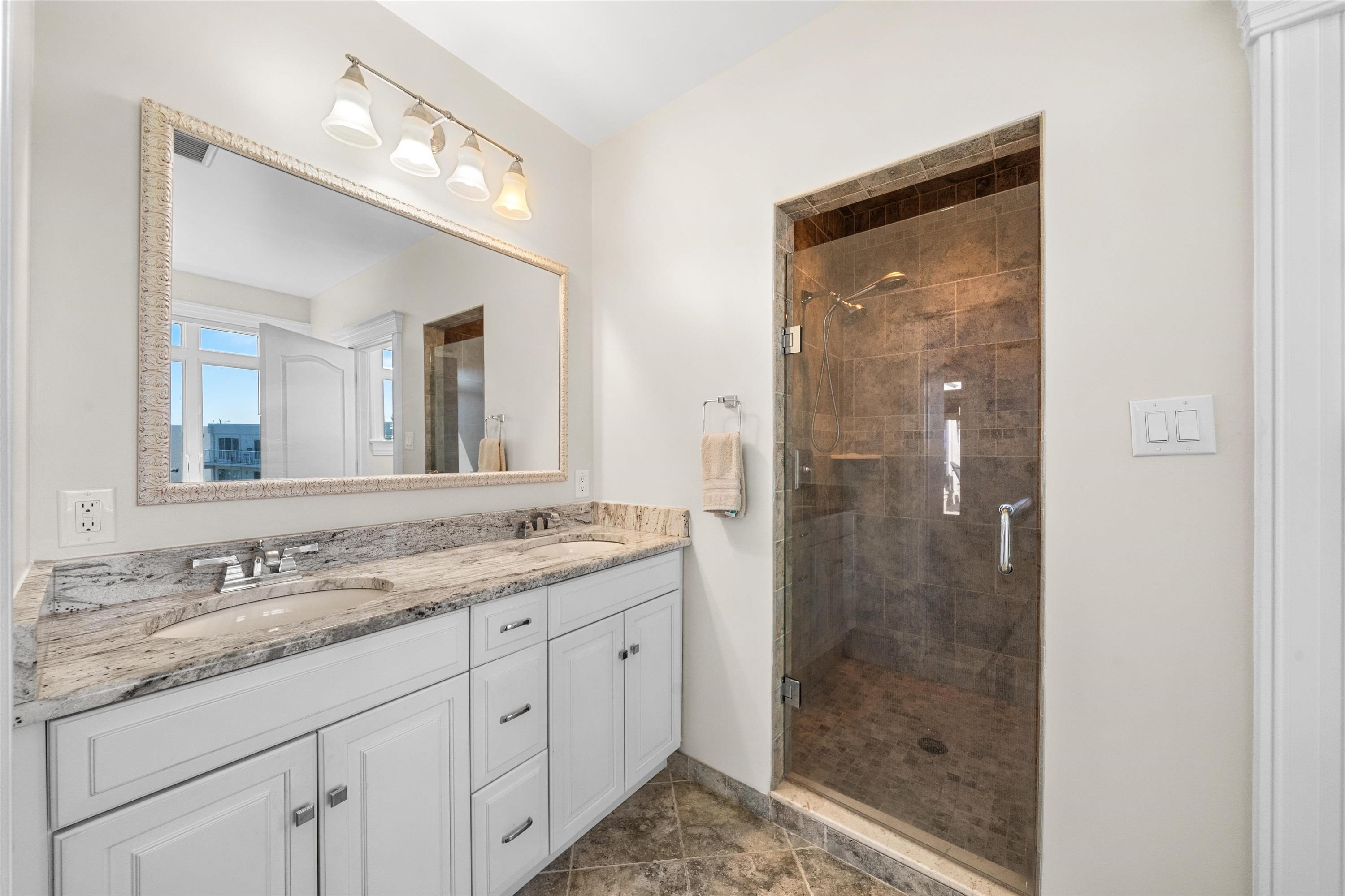 Bathroom with a double-sink vanity and glass-enclosed brown tile shower.