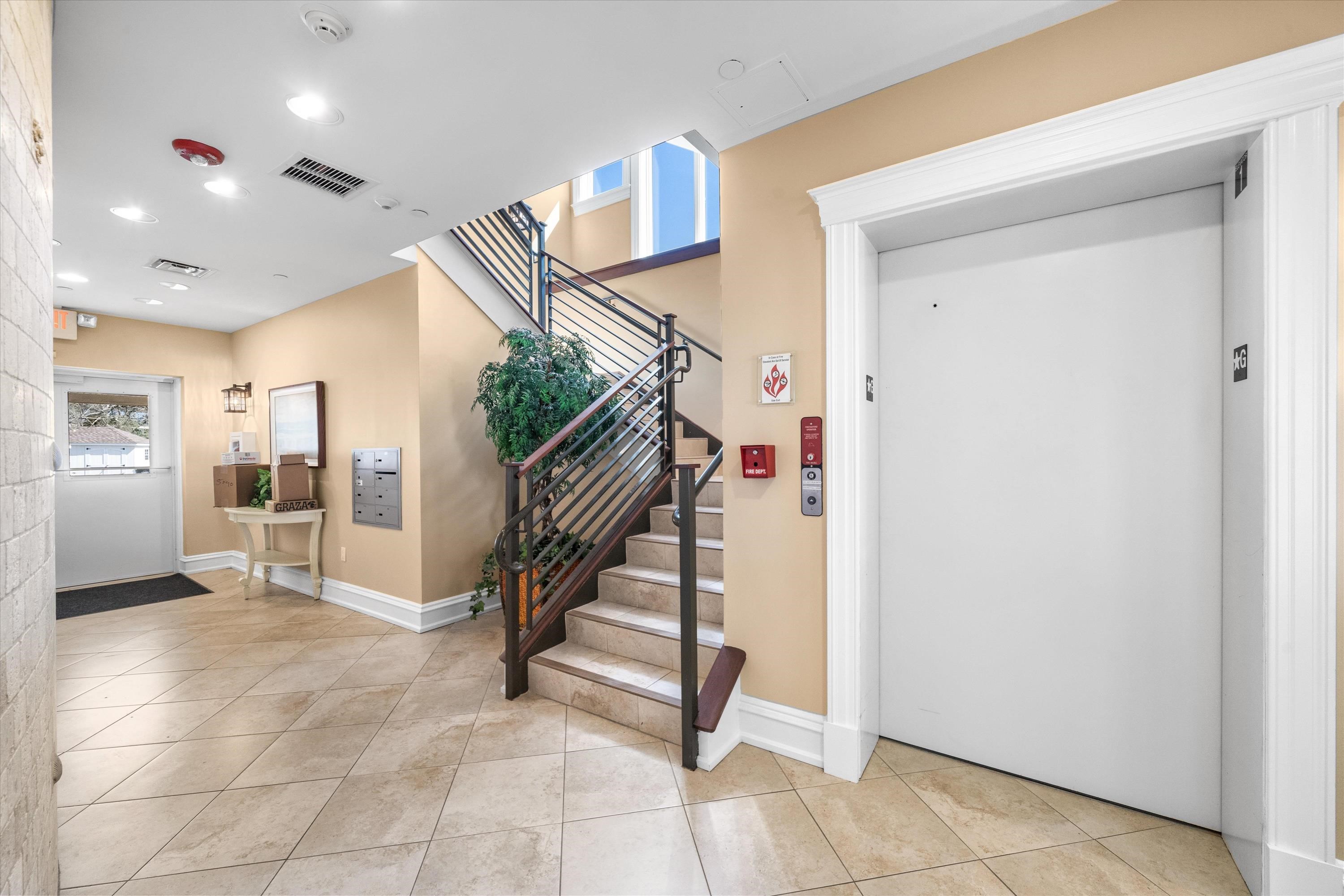 Condominium lobby with a large elevator and tiled staircase with dark railings.