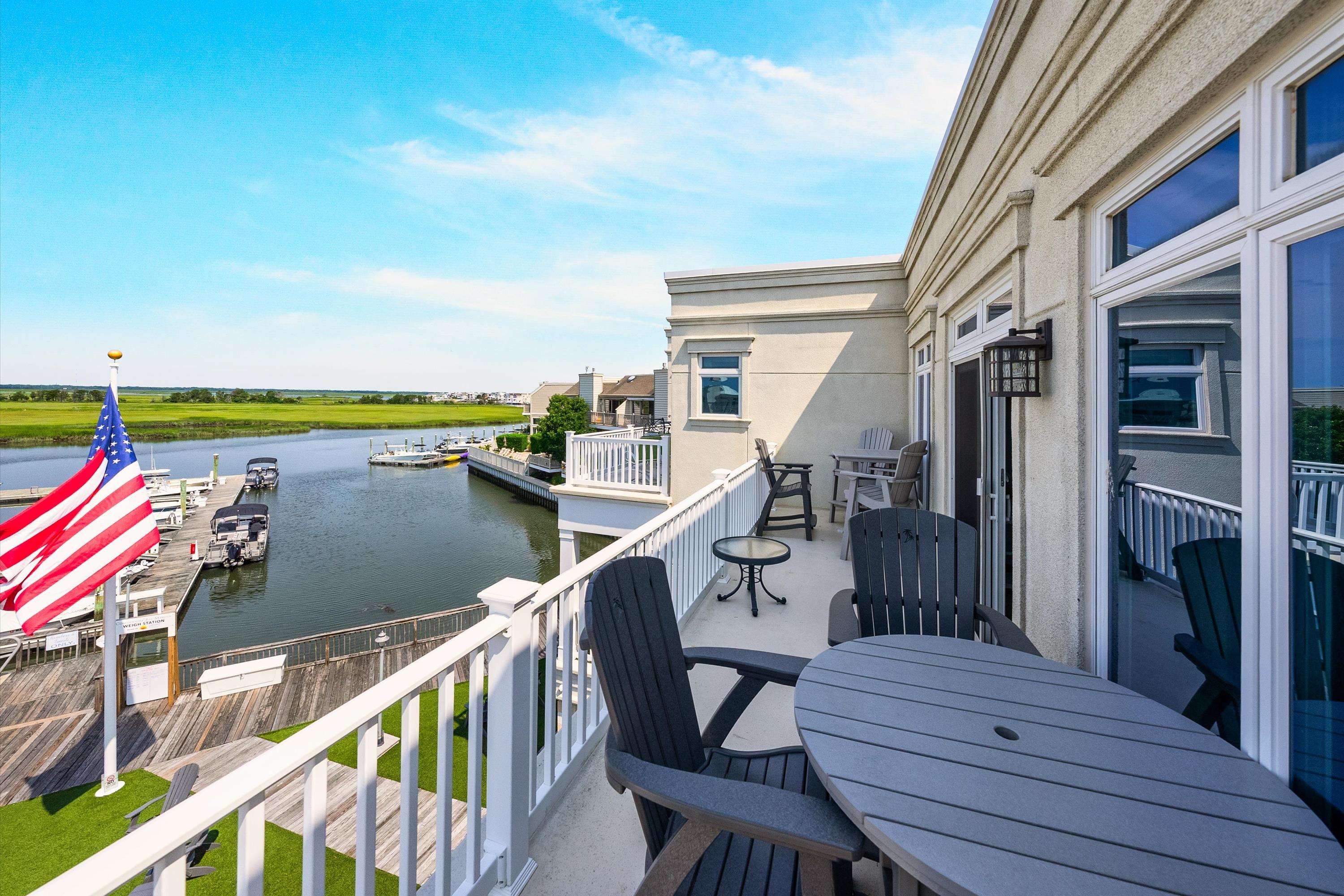 Condo balcony overlooking a marina canal, with patio dining set, Adirondack chairs, and an American flag.